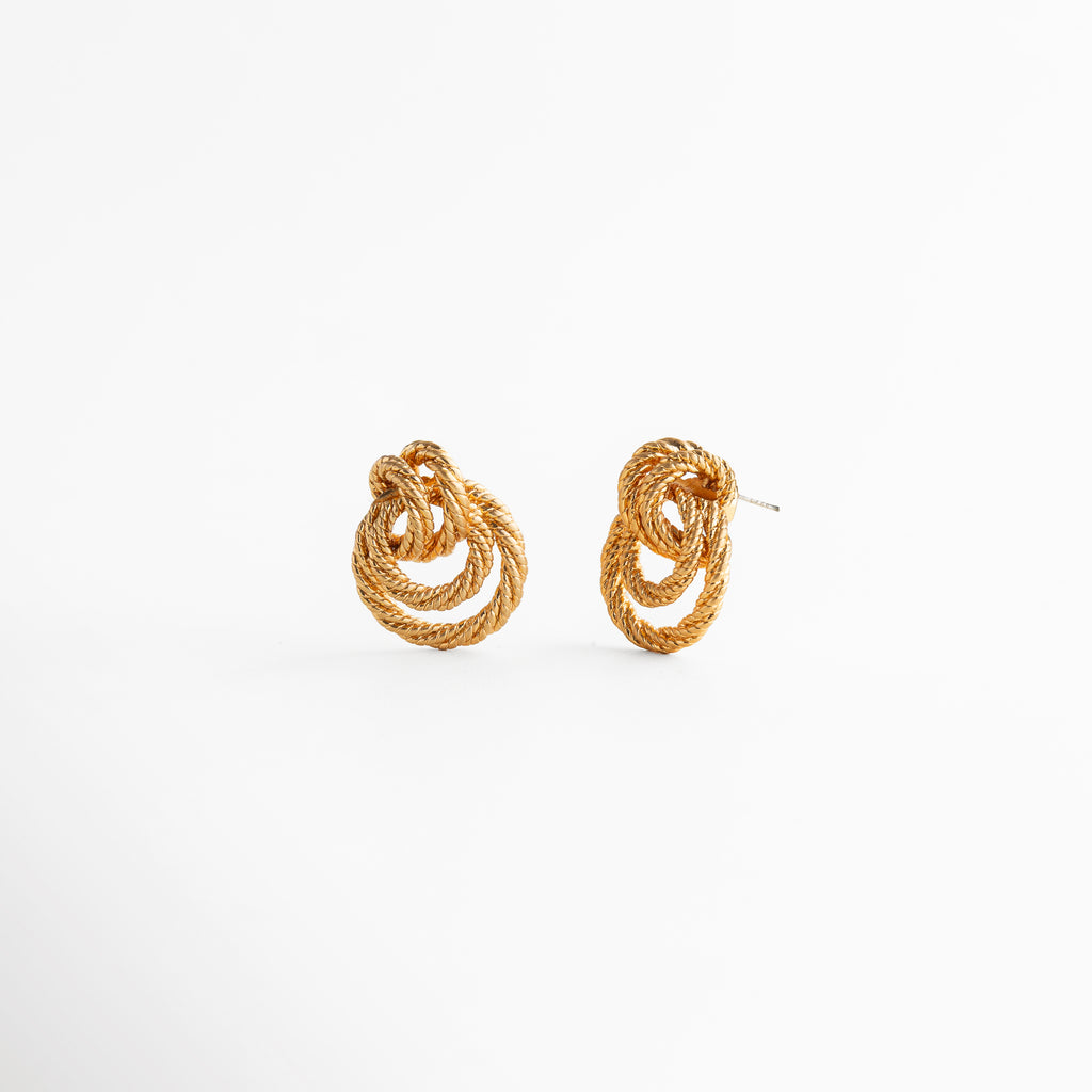 aretes dorados con diseño tridimensional entrelazado, vista lateral de aretes con relieve y textura marcada, aretes compactos con estructura curva y elegante, joyería dorada con diseño escultórico y profundidad, aretes de moda con acabado brillante y forma envolvente
