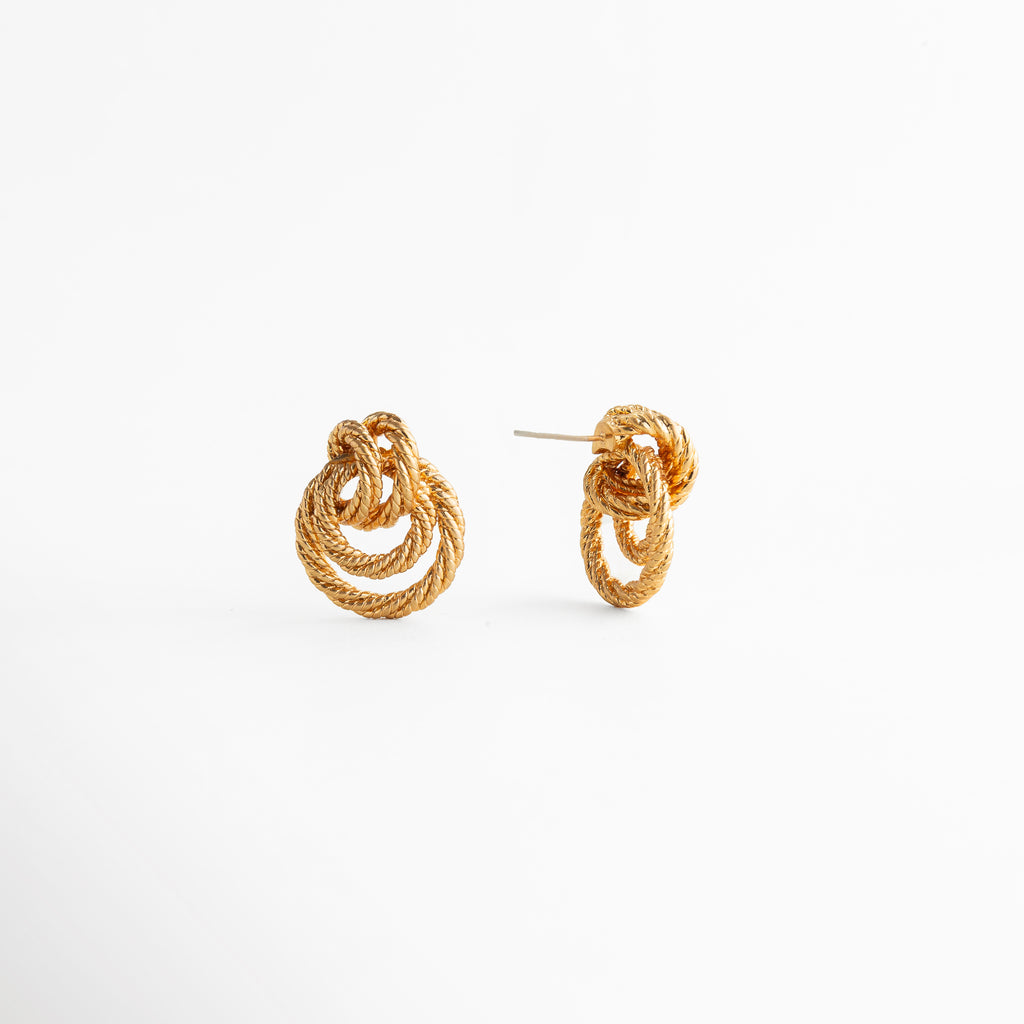 detalle de aretes dorados con textura fina, acercamiento a aretes entrelazados con acabado brillante, joyería dorada con diseño orgánico y líneas suaves, detalle de aretes statement con volumen delicado, aretes elegantes con inspiración artesanal