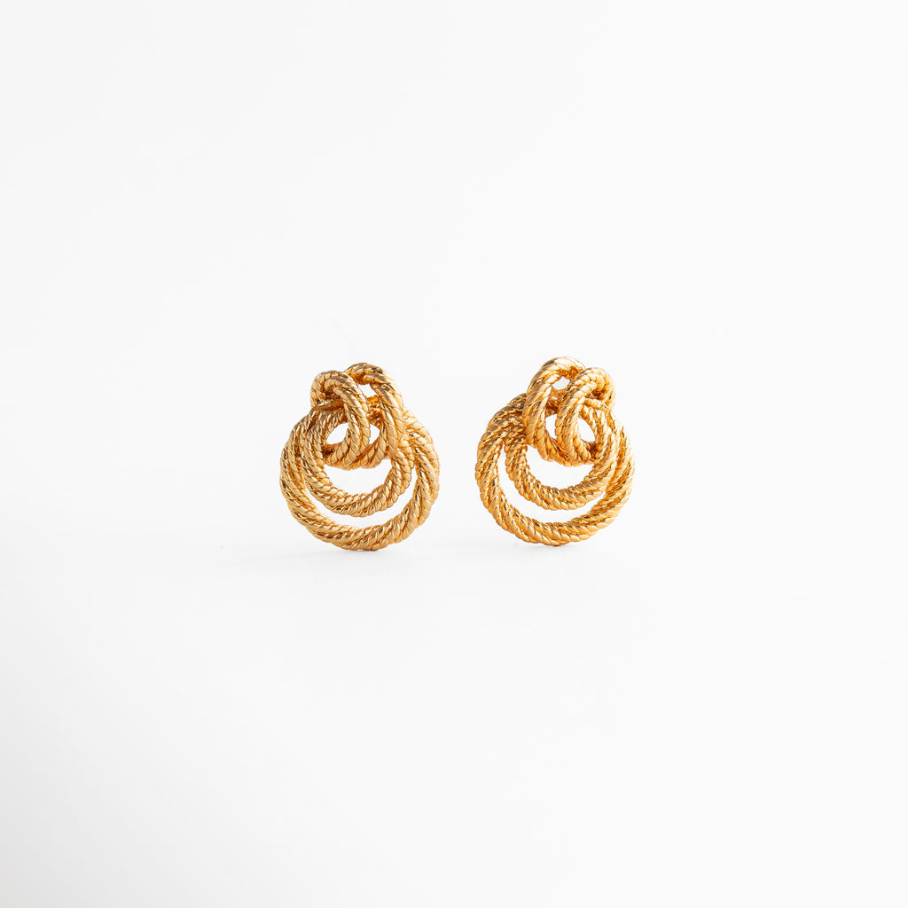 aretes dorados con diseño entrelazado de forma orgánica, aretes statement pequeños con acabado texturizado, joyería elegante con curvas entrelazadas y brillo sutil, aretes tipo nudo dorado de estilo sofisticado, aretes modernos con volumen y detalle artesanal
