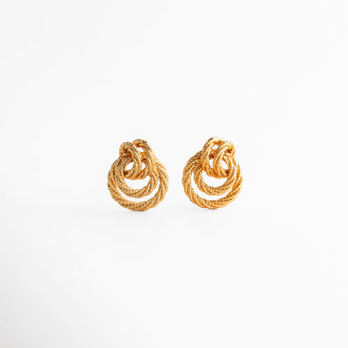 aretes dorados con diseño entrelazado de forma orgánica, aretes statement pequeños con acabado texturizado, joyería elegante con curvas entrelazadas y brillo sutil, aretes tipo nudo dorado de estilo sofisticado, aretes modernos con volumen y detalle artesanal