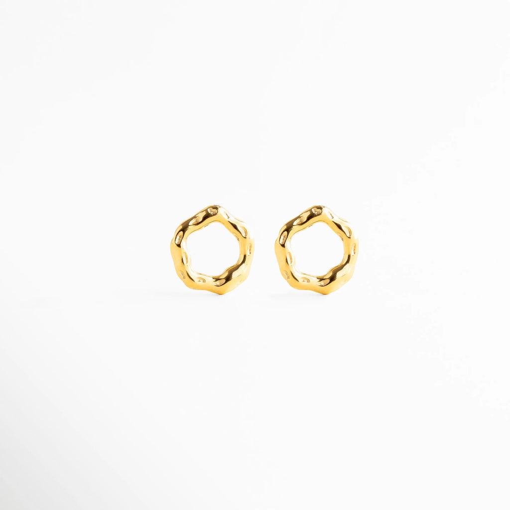 Arete stud mostrando grosor y volumen del diseño, Arete dorado con silueta irregular desde perfil, Detalle lateral de arete circular orgánico, Arete pequeño con diseño moderno tridimensional, Stud elegante con acabado pulido