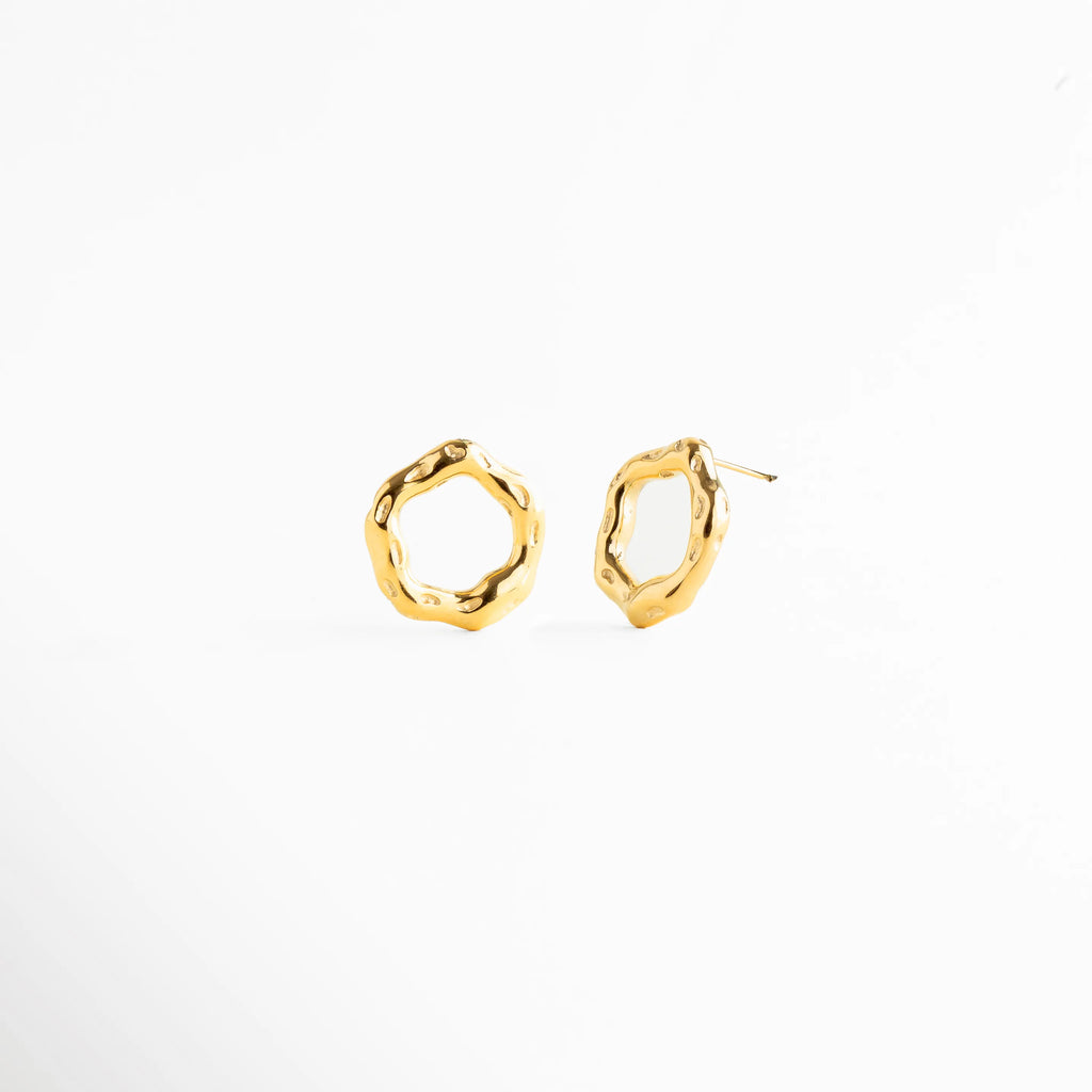 Aretes tipo stud con diseño circular irregular de acabado pulido, Aretes dorados de forma orgánica y estética moderna, Aretes pequeños con silueta abstracta y elegante, Studs dorados minimalistas con diseño artesanal, Aretes de aro irregular en joyería contemporánea