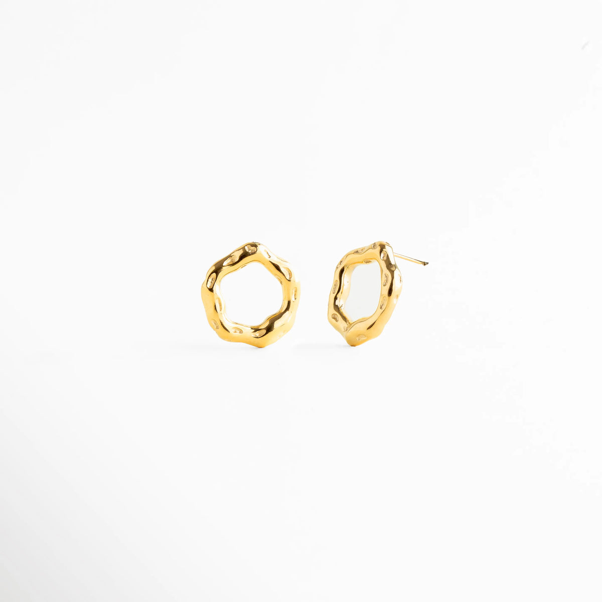 Aretes tipo stud con diseño circular irregular de acabado pulido, Aretes dorados de forma orgánica y estética moderna, Aretes pequeños con silueta abstracta y elegante, Studs dorados minimalistas con diseño artesanal, Aretes de aro irregular en joyería contemporánea