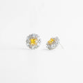 aretes plateados con piedra central amarilla brillante, aretes elegantes con zirconias y centro amarillo, aretes tipo stud con halo de zirconias plateadas, joyería fina con piedra amarilla enmarcada, aretes sofisticados con contraste plateado y amarillo, aretes clásicos con brillo intenso