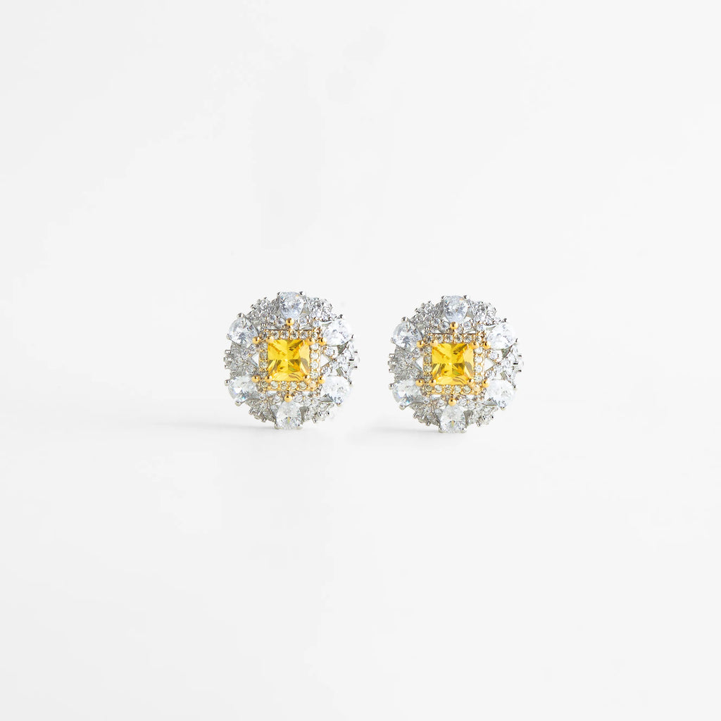 aretes plateados con piedra amarilla vista lateral, aretes con montura elevada y zirconias brillantes, detalle de aretes con halo de zirconias, aretes elegantes con estructura refinada, aretes con acabado brillante y piedra central, joyería delicada con volumen sutil