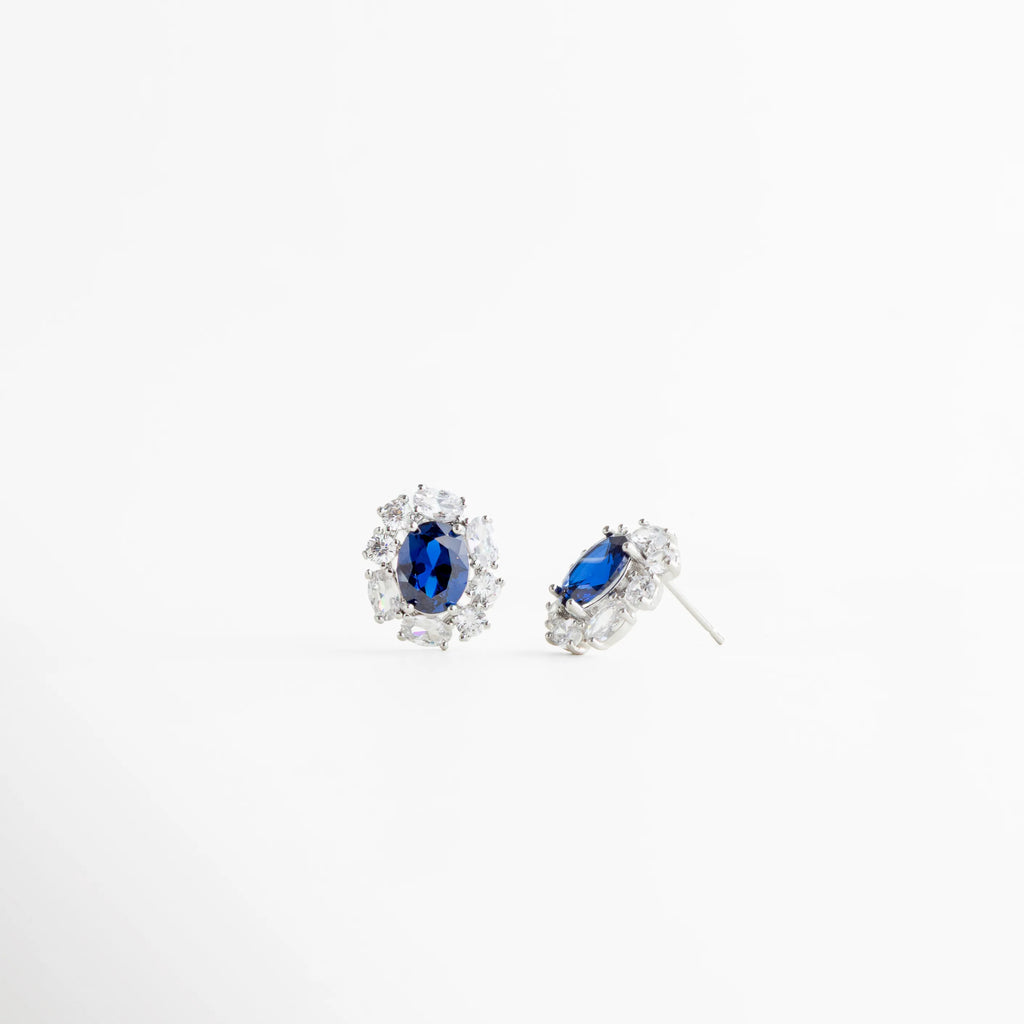 Aretes stud plateados con poste y broche de presión, Detalle lateral de aretes con piedra azul oscuro, Cierre trasero de aretes plateados elegantes, Aretes pequeños con estructura fina y pulida, Vista lateral de aretes con zirconias brillantes, Aretes cómodos y ligeros de uso diario