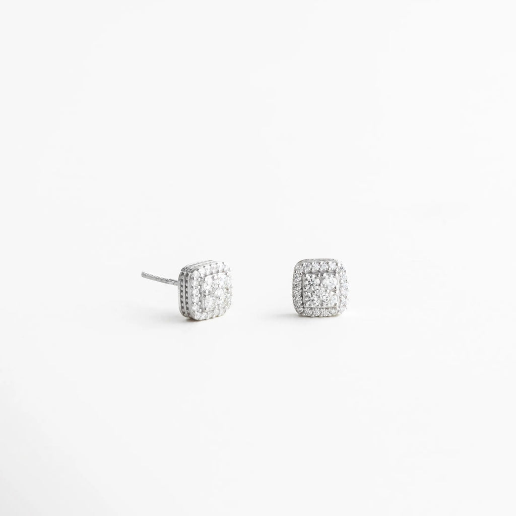 Aretes plateados pequeños vistos en ángulo con textura brillante, Studs delicados plateados con zirconias desde vista lateral, Aretes minimalistas plateados con diseño cuadrado elegante, Aretes pequeños plateados para combinación en ear stack, Studs plateados con brillo suave y diseño atemporal, Aretes discretos plateados para uso diario