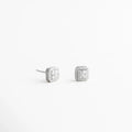 Aretes plateados pequeños vistos en ángulo con textura brillante, Studs delicados plateados con zirconias desde vista lateral, Aretes minimalistas plateados con diseño cuadrado elegante, Aretes pequeños plateados para combinación en ear stack, Studs plateados con brillo suave y diseño atemporal, Aretes discretos plateados para uso diario