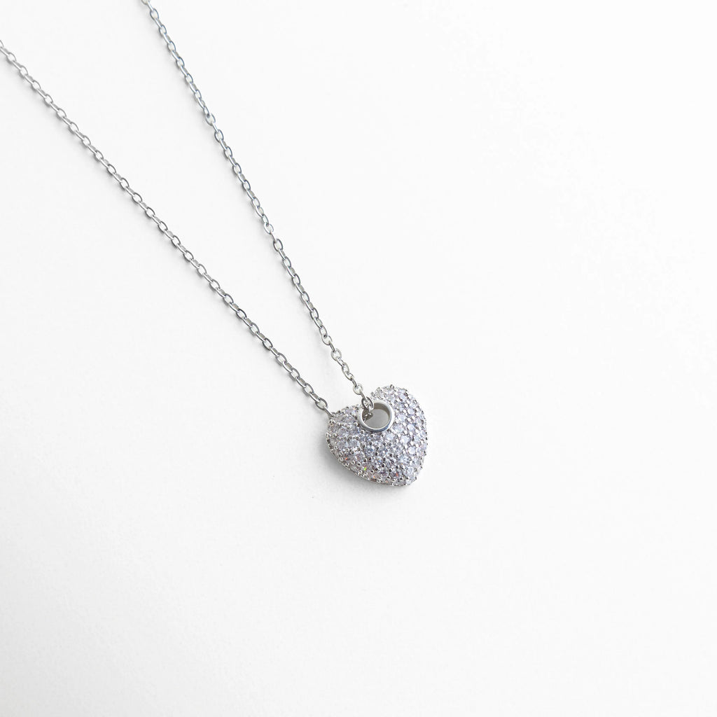 Dije de corazón con zirconias engastadas, acabado en oro blanco 14K, Detalle de collar con dije de corazón brillante con zirconias, Corazón de zirconias en collar fino, diseño elegante y moderno, Close up de dije en forma de corazón con piedras brillantes, Dije delicado con zirconias sobre base de cobre, estilo sofisticado