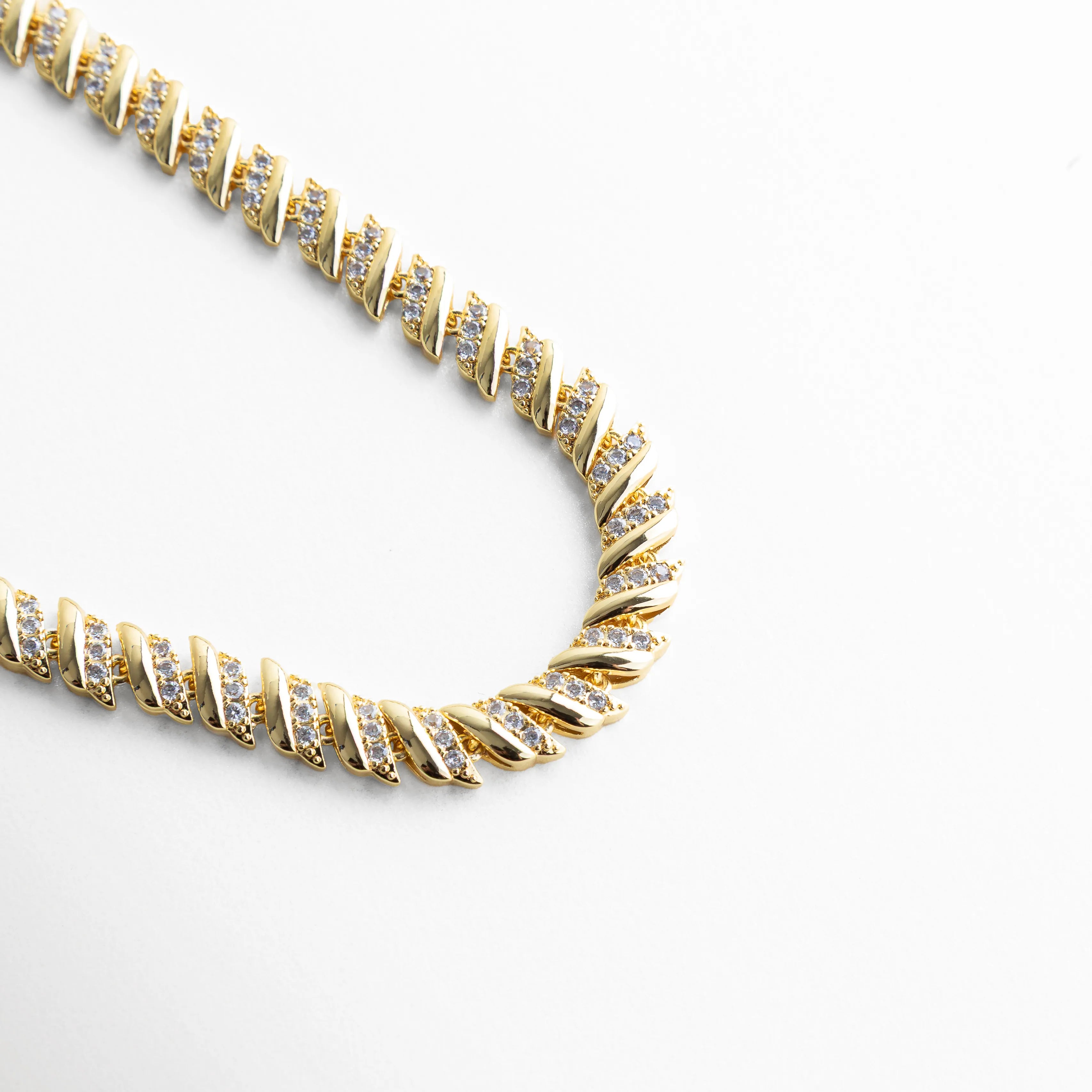 Vista curva de collar dorado con zirconias brillantes, Collar Brock en forma curvada mostrando su diseño flexible, Vista lateral de collar con acabado en oro 18K, Collar con zirconias CZ en ángulo elegante, Diseño curvo de collar con brillo uniforme