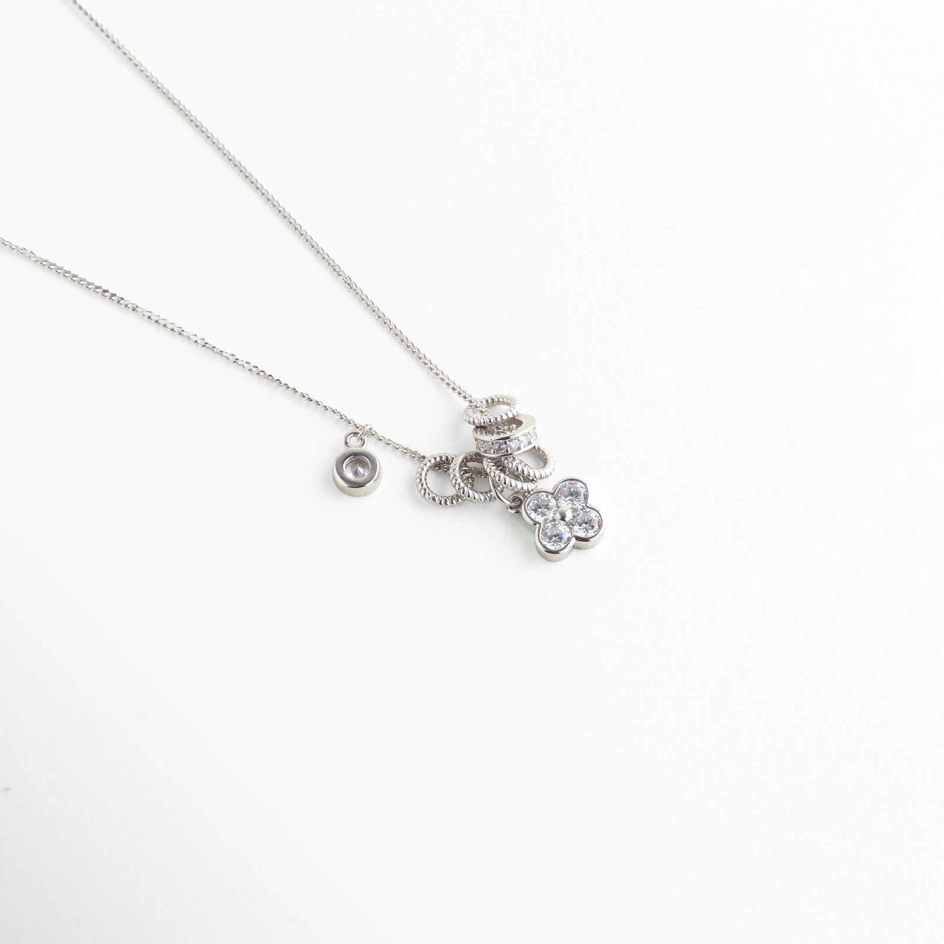 Collar de Plata Ley 925 con dijes colgantes de trébol y aros con zirconias, Gargantilla de plata con dije de flor de cuatro pétalos y zirconias brillantes, Detalle de collar con múltiples charms de plata ley 925 y pedrería fina, Joyería de plata con recubrimiento enchapado y colgantes de zirconias cristalinas, Collar estilo "charms" en plata con charms circulares y trébol de zirconias.