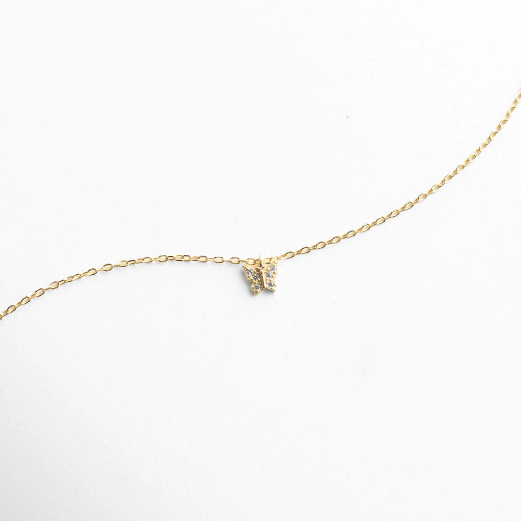 Collar dorado con dije pequeño en forma de mariposa con zirconias brillantes, reflejando elegancia y sutileza.