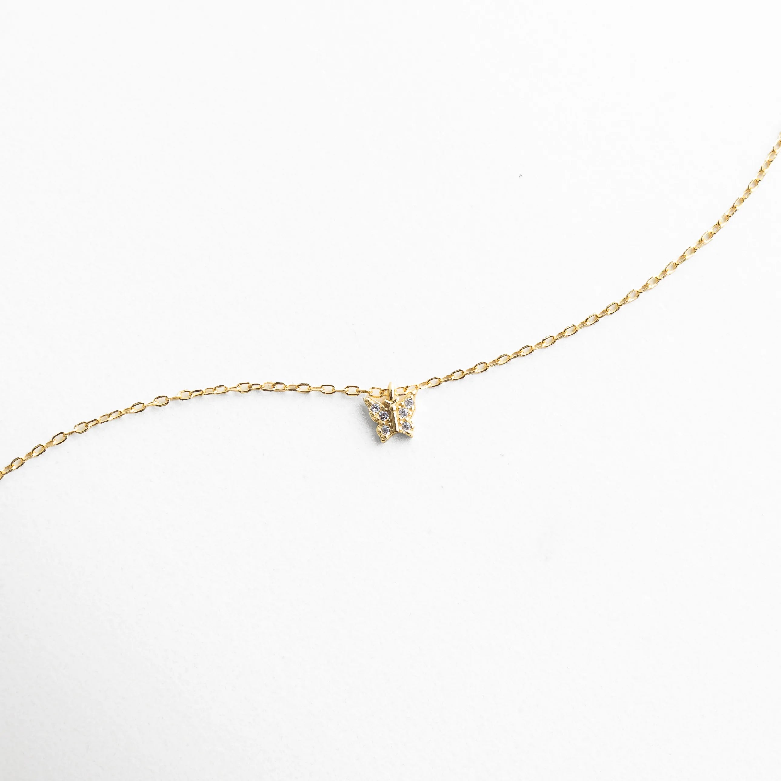 Collar dorado con dije pequeño en forma de mariposa con zirconias brillantes, reflejando elegancia y sutileza.