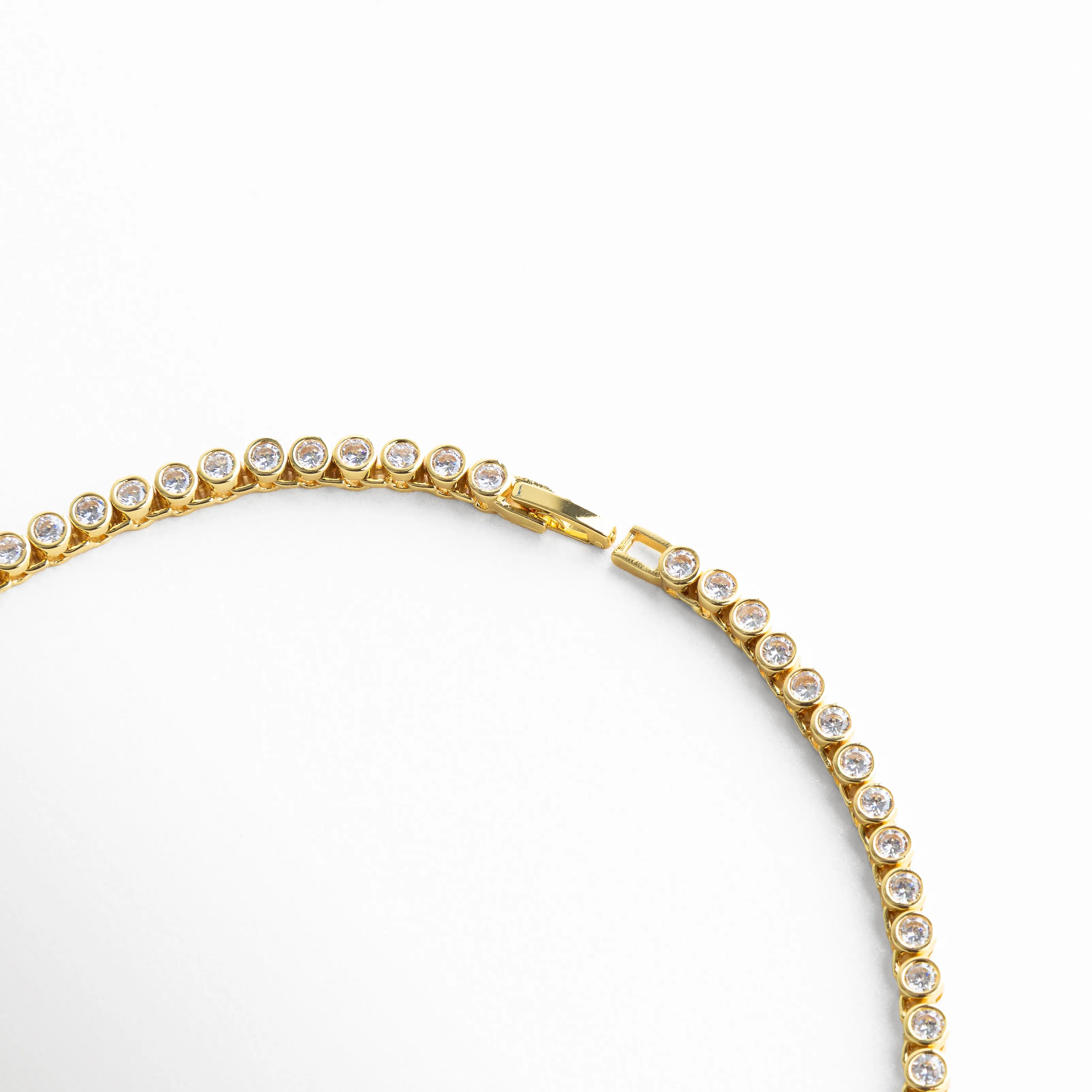 Detalle de collar dorado con zirconias brillantes en forma curva, Primer plano de collar con piedras zirconia y acabado en oro 18K, Acercamiento a collar con diseño fino y brillo elegante, Vista curva de collar con zirconias alineadas, Detalle elegante de collar con incrustaciones brillantes