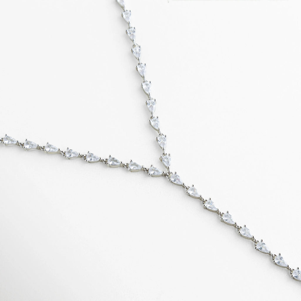 detalle de collar lariat plateado, caída frontal del collar estilo lariat, joyería elegante con acabado pulido, collar plateado con diseño refinado, collar minimalista de estética contemporánea, collar largo con terminación delicada