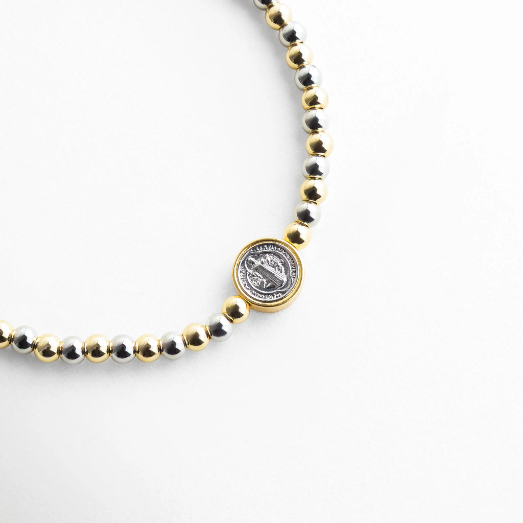 Detalle de pulsera con dije central y cuentas en oro blanco 18K, Close up de pulsera ajustable con pieza central elegante, Pulsera con medalla decorativa y cuentas metálicas en acabado dorado, Detalle central de pulsera con diseño sofisticado en oro y oro blanco, Pulsera artesanal con dije redondo y acabado brillante