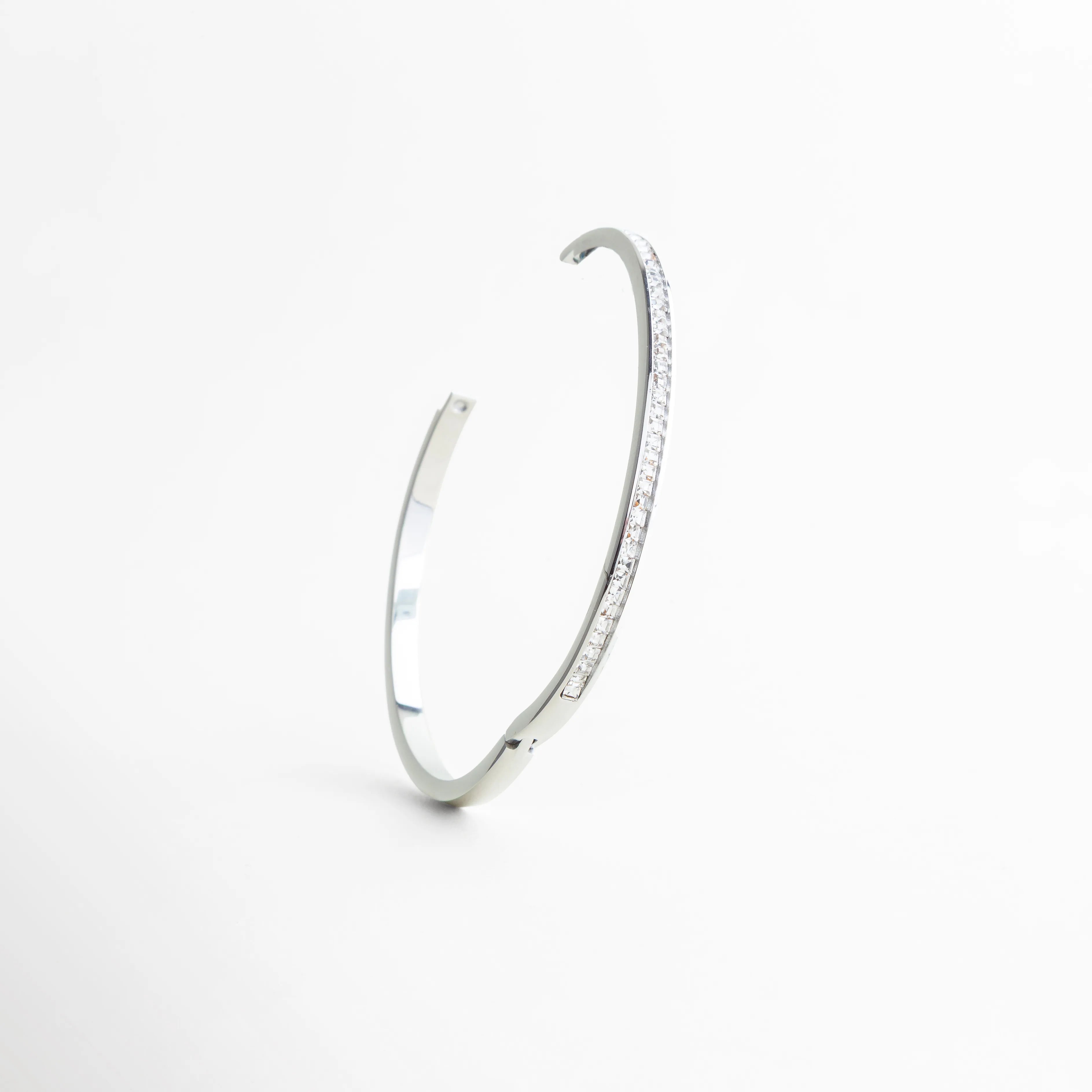 pulsera plateada vista en ángulo elegante, pulsera rígida con brillo sutil, pulsera de zirconias diseño moderno, pulsera minimal vista diagonal, pulsera elegante joyería contemporánea, pulsera plateada con acabado pulido
