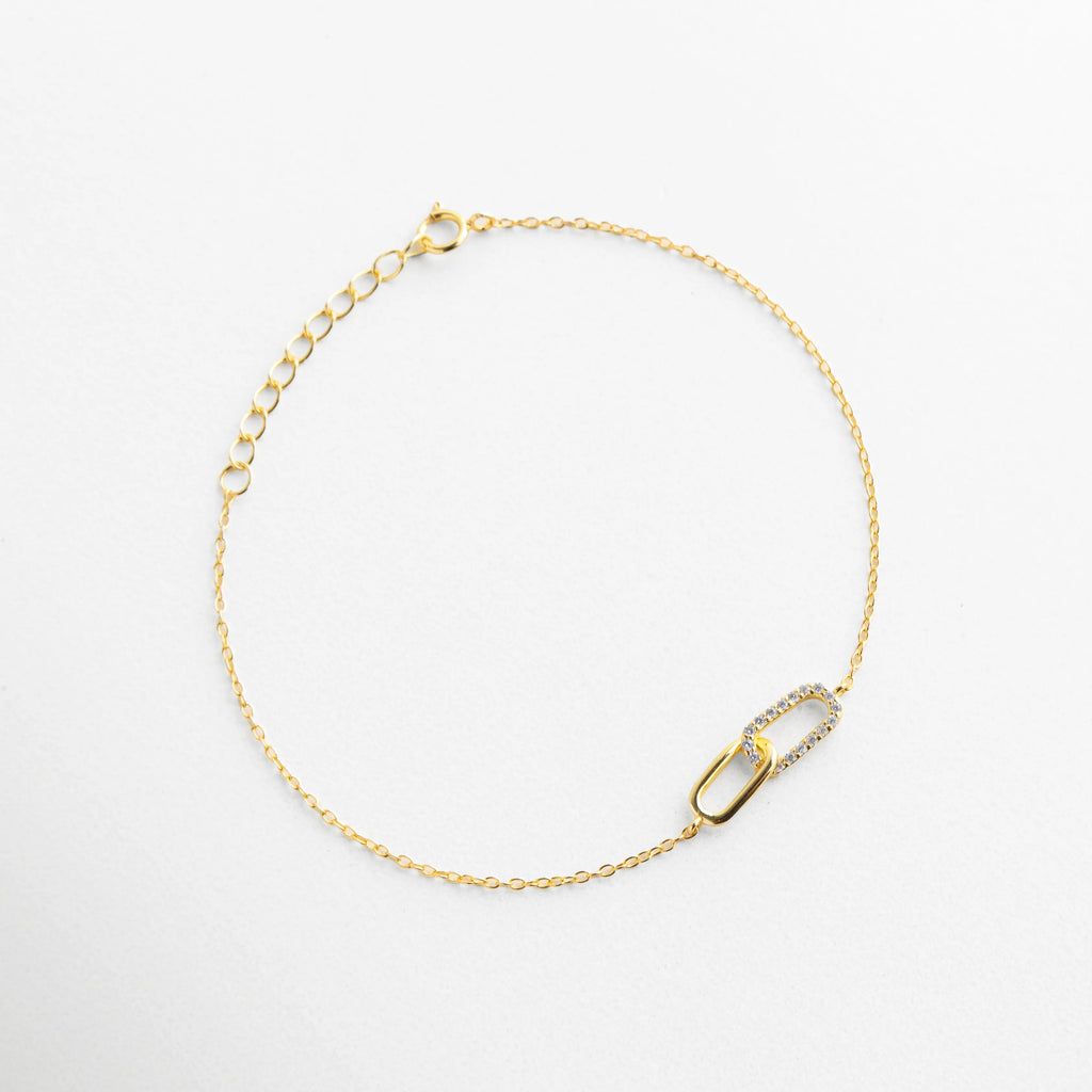 Pulsera circular de plata dorada de 17 cm con dije central de eslabones y circonias, Composición completa de pulsera de cadena delgada con acabado en oro y piedras brillantes, Brazalete fino de plata con diseño de eslabones cruzados, vista de producto completa, Pulsera de oro sobre plata con extensor de 3 cm y detalle central de lujo, Accesorio de muñeca elegante y sencillo con dije de eslabón empedrado de circonias.