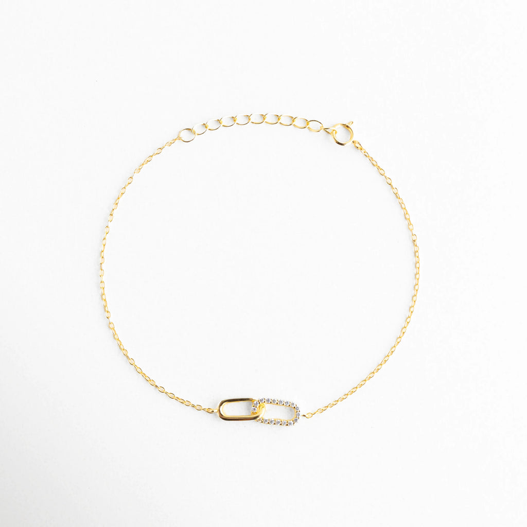 Vista aérea de pulsera de eslabones entrelazados con circonias y cadena dorada, Pulsera de diseño "Interlocking" en plata 925 con destellos de micro-circonias, Joyería minimalista: pulsera de cadena fina con detalle central asimétrico brillante, Brazalete dorado con dije de unión simbólica, ideal para regalo de aniversario o amistad, Perspectiva superior de pulsera de plata dorada resaltando la finura de la cadena.