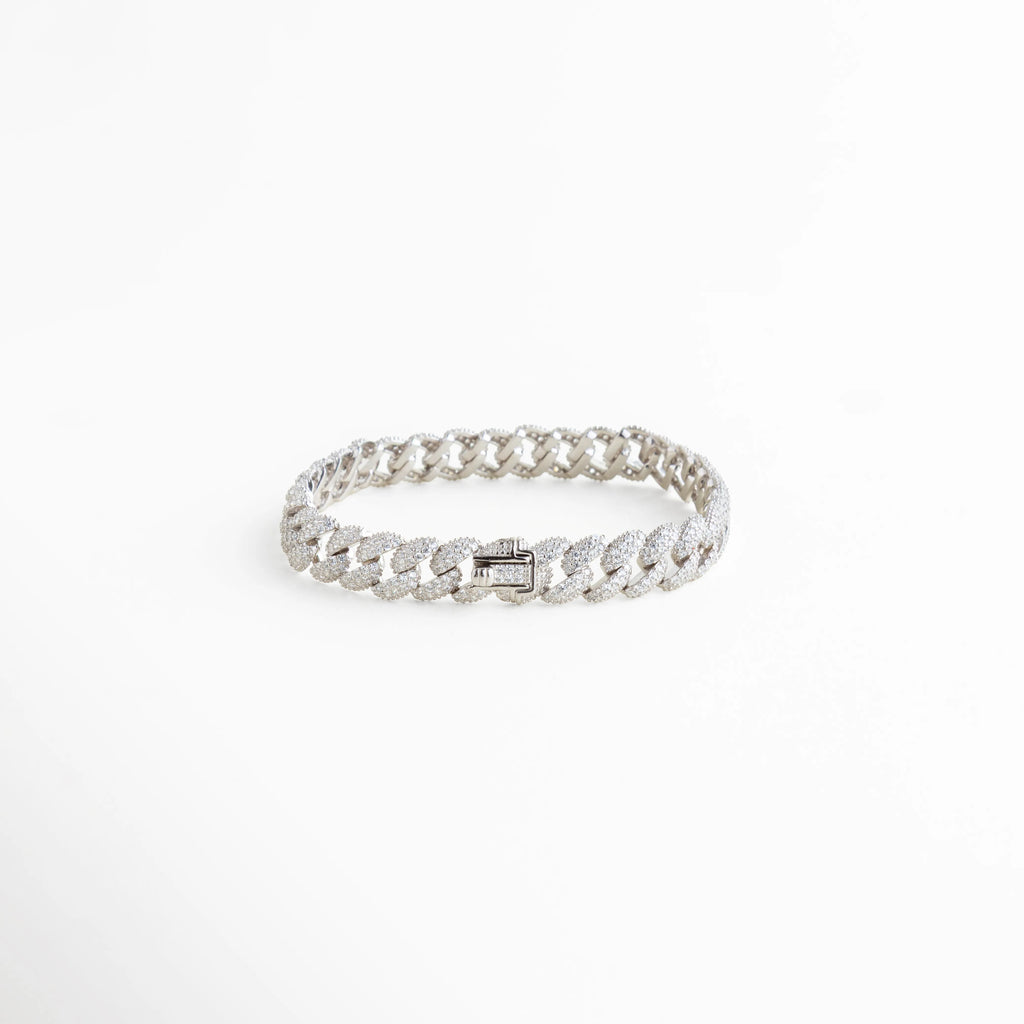 Vista lateral de pulsera cubana de plata 925 mostrando el broche de caja con seguridad, Detalle de eslabones cubanos con diamantes sintéticos y acabado pulido en oro blanco 18k, Pulsera de cadena brillante con diseño de eslabón plano y cierre reforzado, Perspectiva de brazalete estilo "iced out" en plata ley 925 con pedrería fina, 
Detalle técnico del grosor y la alineación de las piedras en la pulsera cubana.