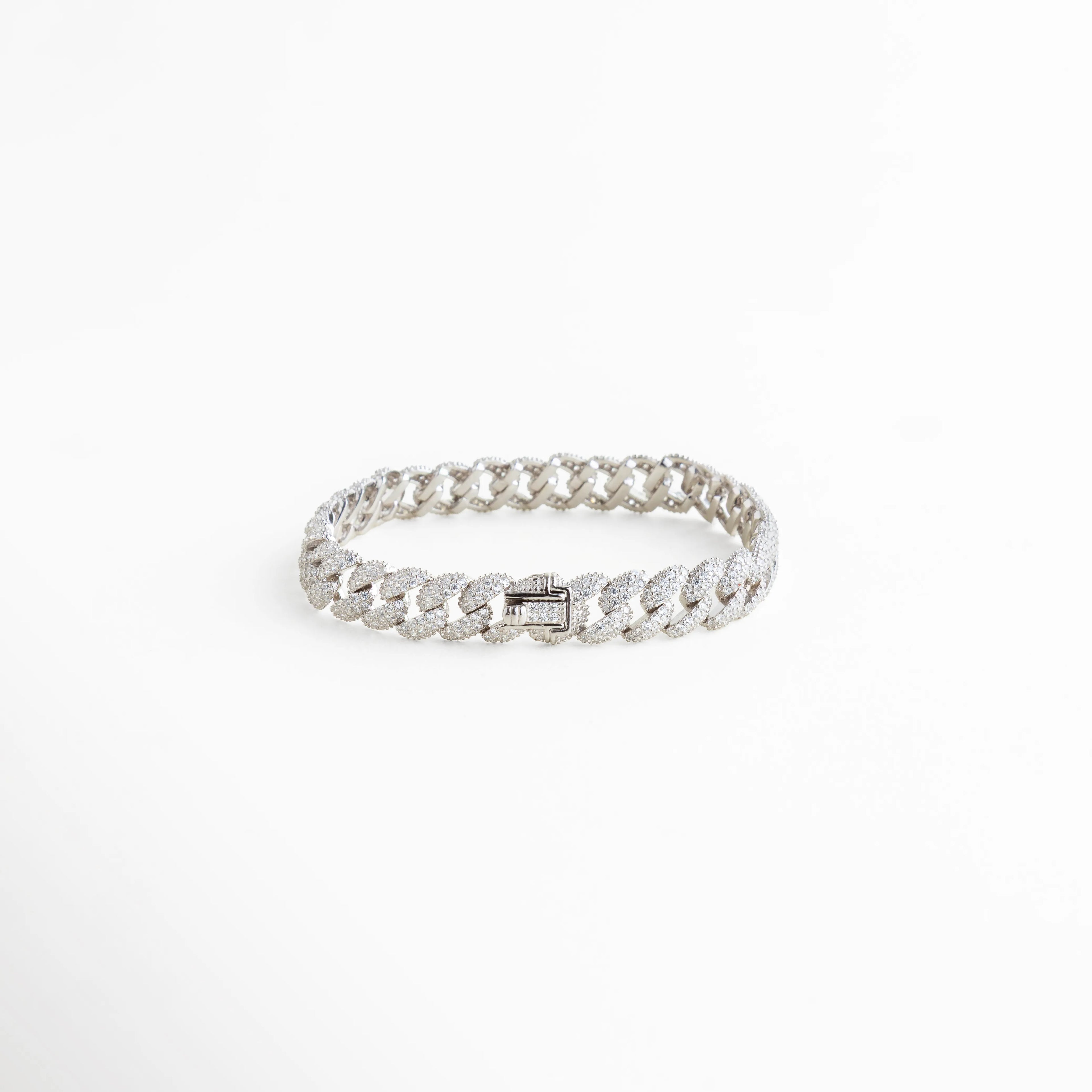 Vista lateral de pulsera cubana de plata 925 mostrando el broche de caja con seguridad, Detalle de eslabones cubanos con diamantes sintéticos y acabado pulido en oro blanco 18k, Pulsera de cadena brillante con diseño de eslabón plano y cierre reforzado, Perspectiva de brazalete estilo "iced out" en plata ley 925 con pedrería fina, 
Detalle técnico del grosor y la alineación de las piedras en la pulsera cubana.