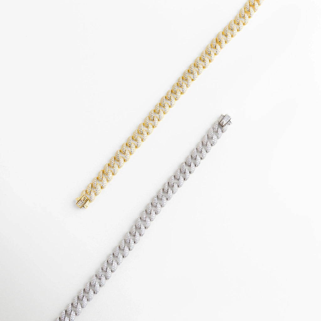 Comparativa de pulseras de eslabón cubano en acabados oro blanco y oro amarillo, Dúo de brazaletes cubanos de plata 925 con diamantes sintéticos en diferentes tonos, Vista de cadenas finas estilo cubano resaltando el contraste de los metales preciosos, Pulseras de lujo con pavé de diamantes sintéticos y recubrimiento enchapado premium, Detalle de eslabones entrelazados en plata ley 925 con brillo excepcional.