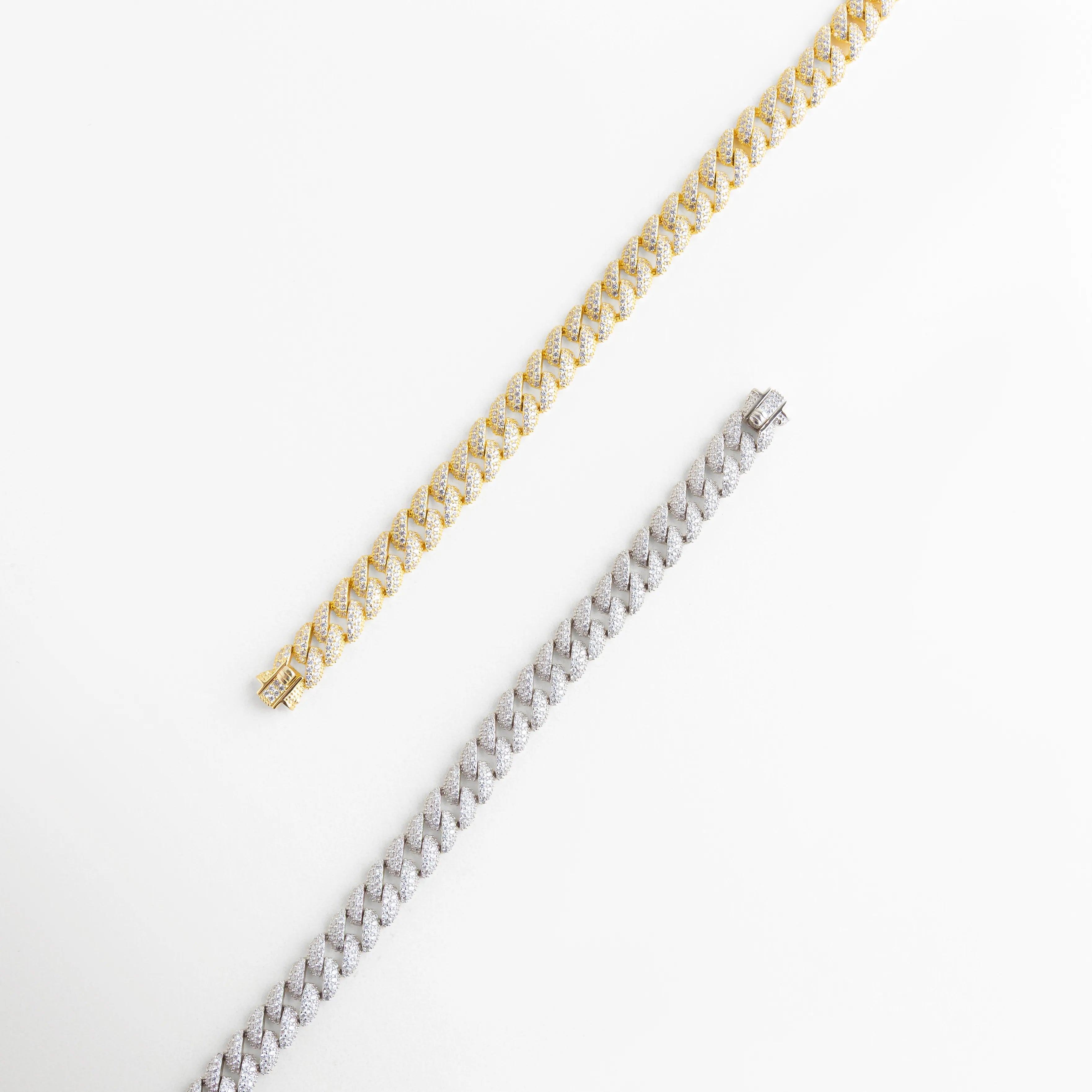 Comparativa de pulseras de eslabón cubano en acabados oro blanco y oro amarillo, Dúo de brazaletes cubanos de plata 925 con diamantes sintéticos en diferentes tonos, Vista de cadenas finas estilo cubano resaltando el contraste de los metales preciosos, Pulseras de lujo con pavé de diamantes sintéticos y recubrimiento enchapado premium, Detalle de eslabones entrelazados en plata ley 925 con brillo excepcional.