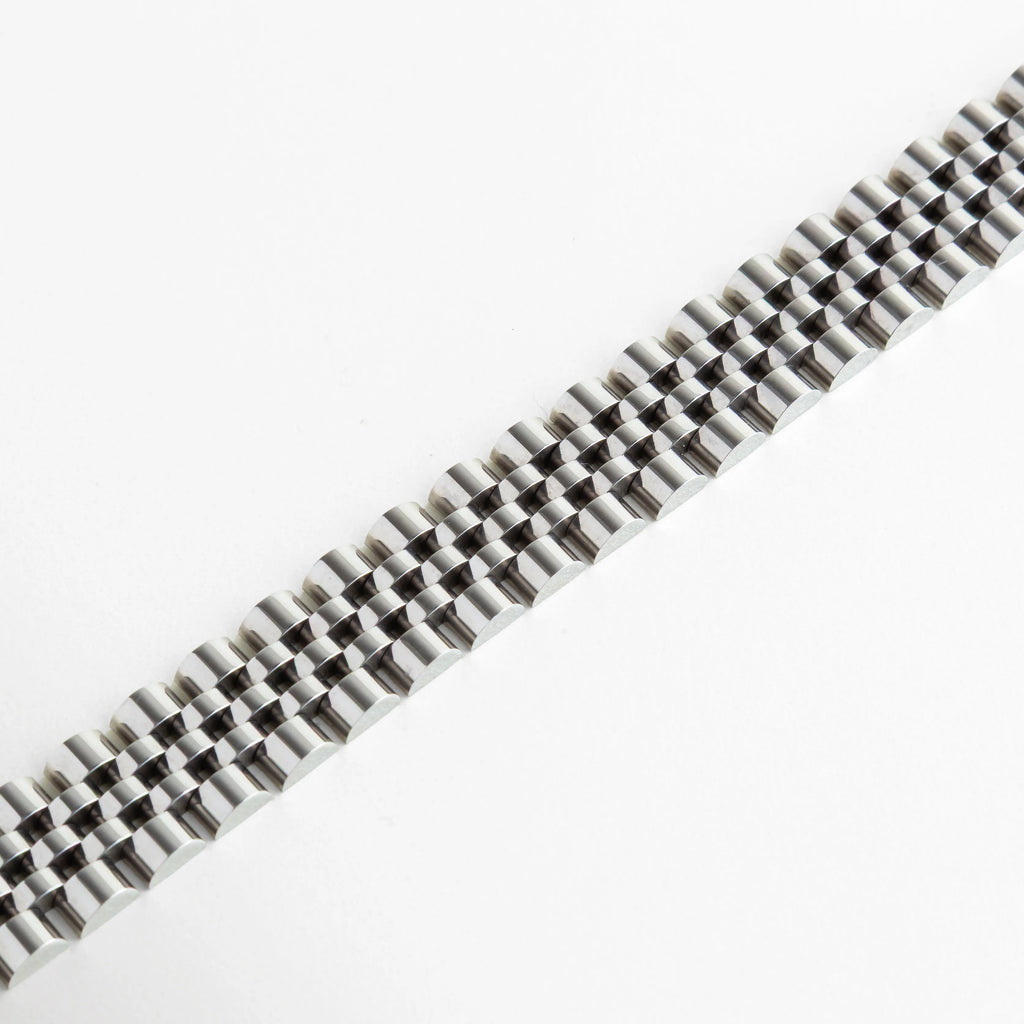 Primer plano de los eslabones articulados de la pulsera mostrando el acabado espejo, Detalle de la textura y el patrón entrelazado del brazalete de 1.5 cm de ancho, Vista macro de pulsera plateada resaltando la precisión del diseño tipo reloj, Estructura de eslabones flexibles con baño de oro blanco de 18K en perspectiva, Detalle de la superficie pulida y resistente de la pulsera metálica plateada.