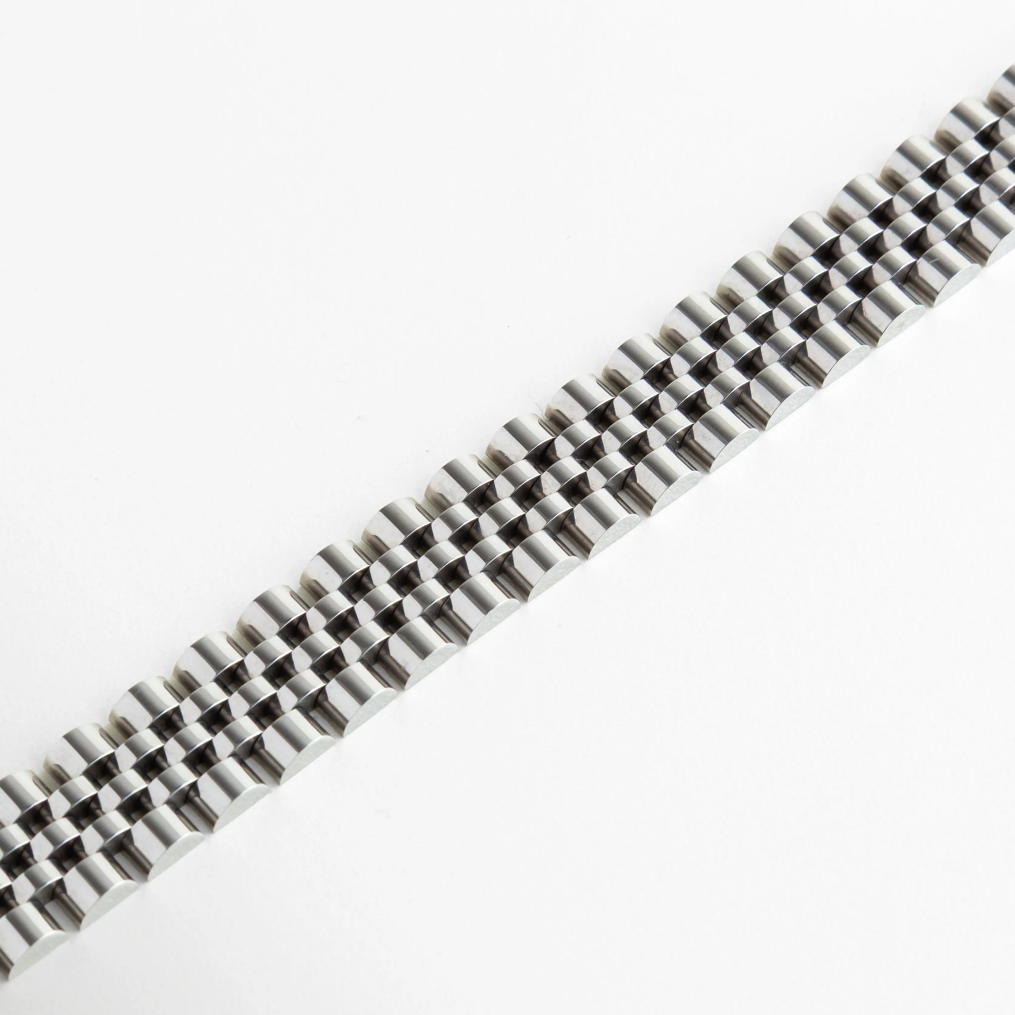 Primer plano de los eslabones articulados de la pulsera mostrando el acabado espejo, Detalle de la textura y el patrón entrelazado del brazalete de 1.5 cm de ancho, Vista macro de pulsera plateada resaltando la precisión del diseño tipo reloj, Estructura de eslabones flexibles con baño de oro blanco de 18K en perspectiva, Detalle de la superficie pulida y resistente de la pulsera metálica plateada.