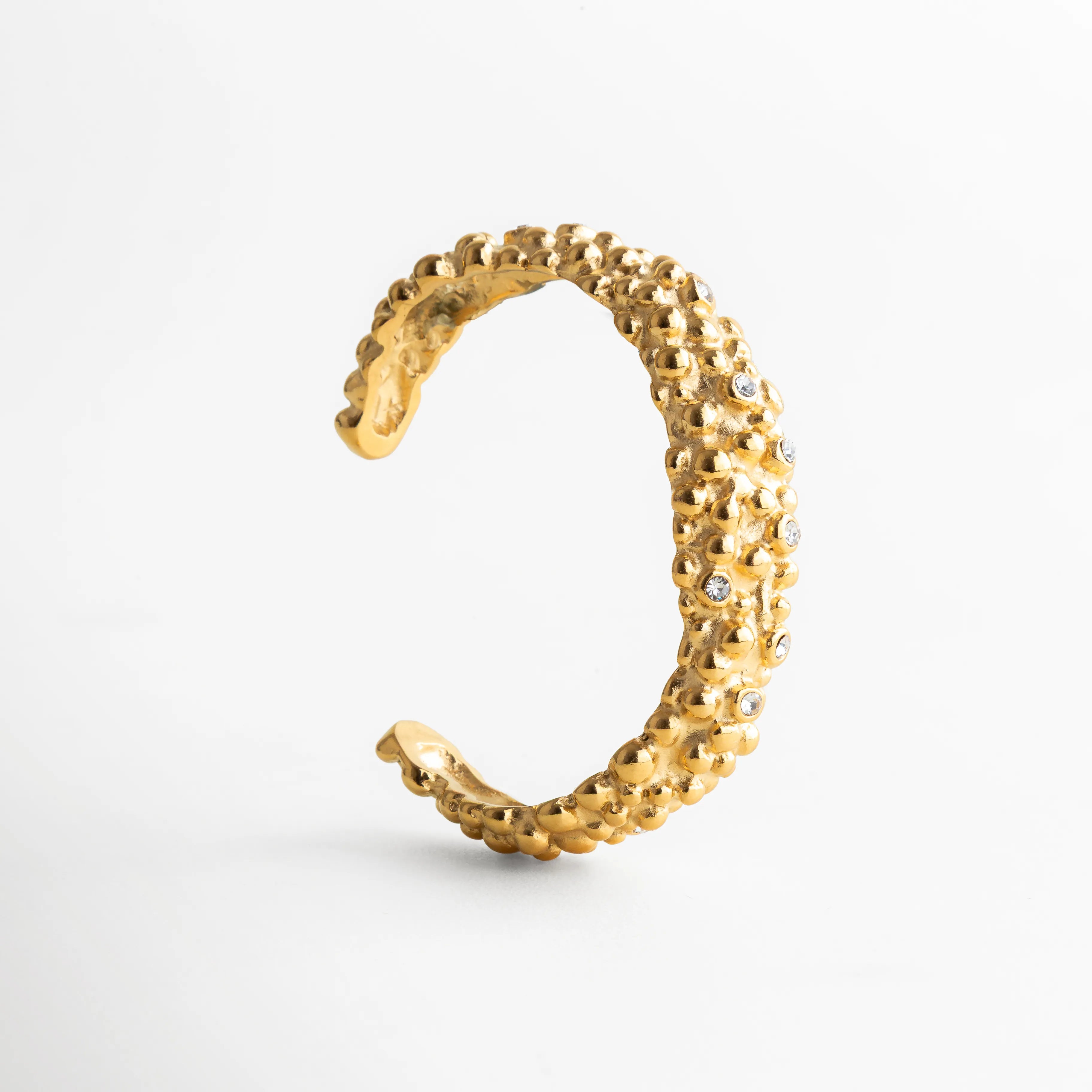 Diseño abierto en acabado dorado brillante con detalles granulados y destellos de zirconias, evocando un estilo artístico y contemporáneo.