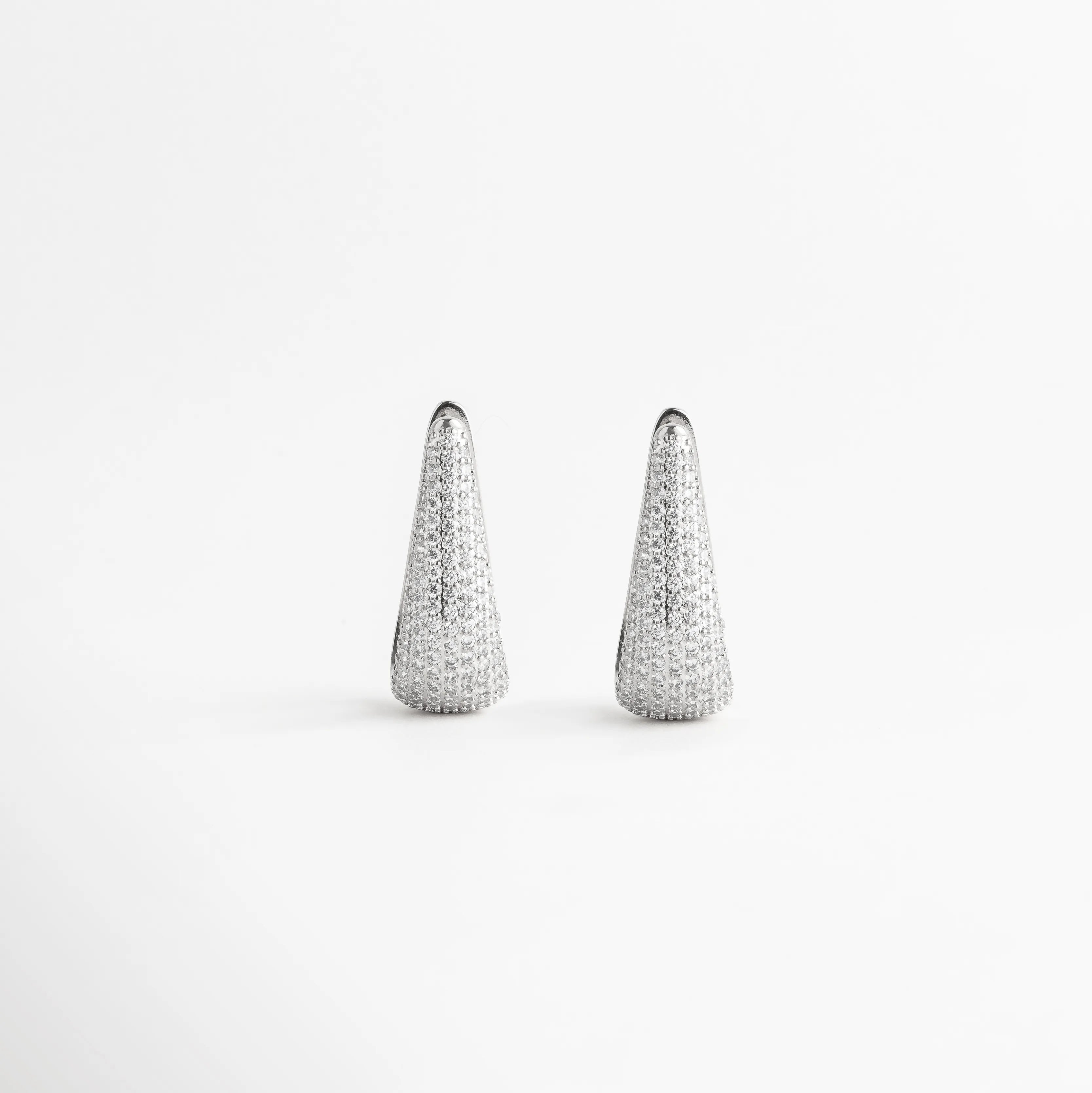 Vista frontal simétrica de aretes alargados con incrustaciones de zirconias brillantes, Par de pendientes de gota modernos en oro blanco 18k para eventos especiales, Arracadas de 4 cm con diseño de punta redondeada y brillo total de zirconias, Joyería contemporánea de cobre enchapado con pedrería fina transparente, Aretes colgantes de silueta orgánica con baño de metal precioso y cristales.