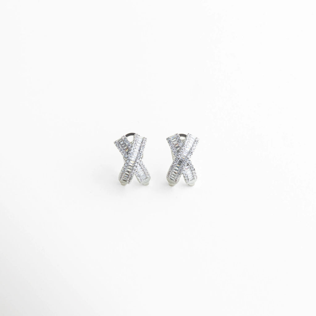 aretes plateados tipo stud con diseño cruzado, aretes en forma de X con zirconias brillantes, aretes pequeños elegantes con acabado plateado, aretes minimalistas con piedras incrustadas, joyería fina aretes cruzados modernos, aretes delicados con brillo sutil frontal