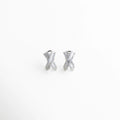 aretes plateados tipo stud con diseño cruzado, aretes en forma de X con zirconias brillantes, aretes pequeños elegantes con acabado plateado, aretes minimalistas con piedras incrustadas, joyería fina aretes cruzados modernos, aretes delicados con brillo sutil frontal