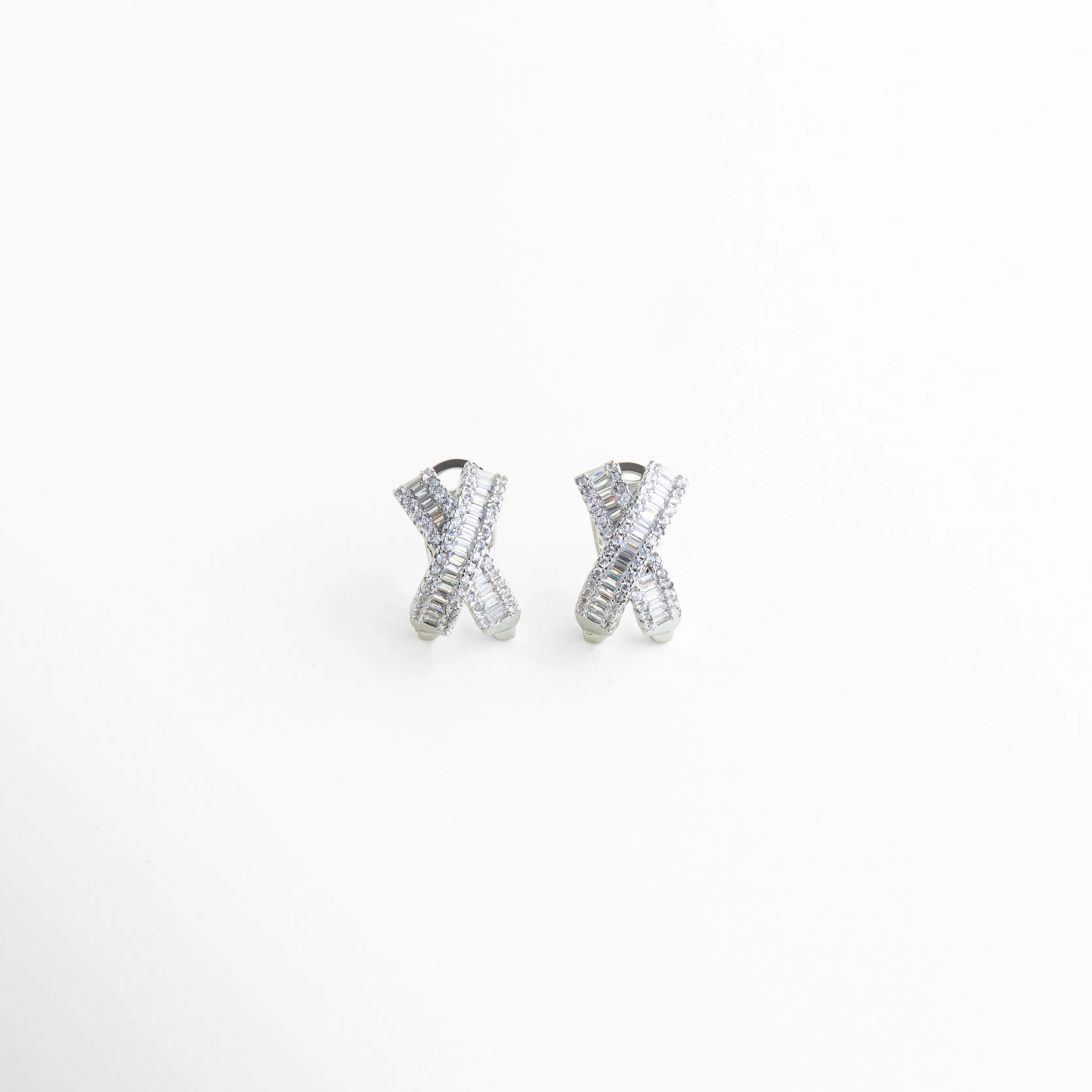aretes plateados tipo stud con diseño cruzado, aretes en forma de X con zirconias brillantes, aretes pequeños elegantes con acabado plateado, aretes minimalistas con piedras incrustadas, joyería fina aretes cruzados modernos, aretes delicados con brillo sutil frontal