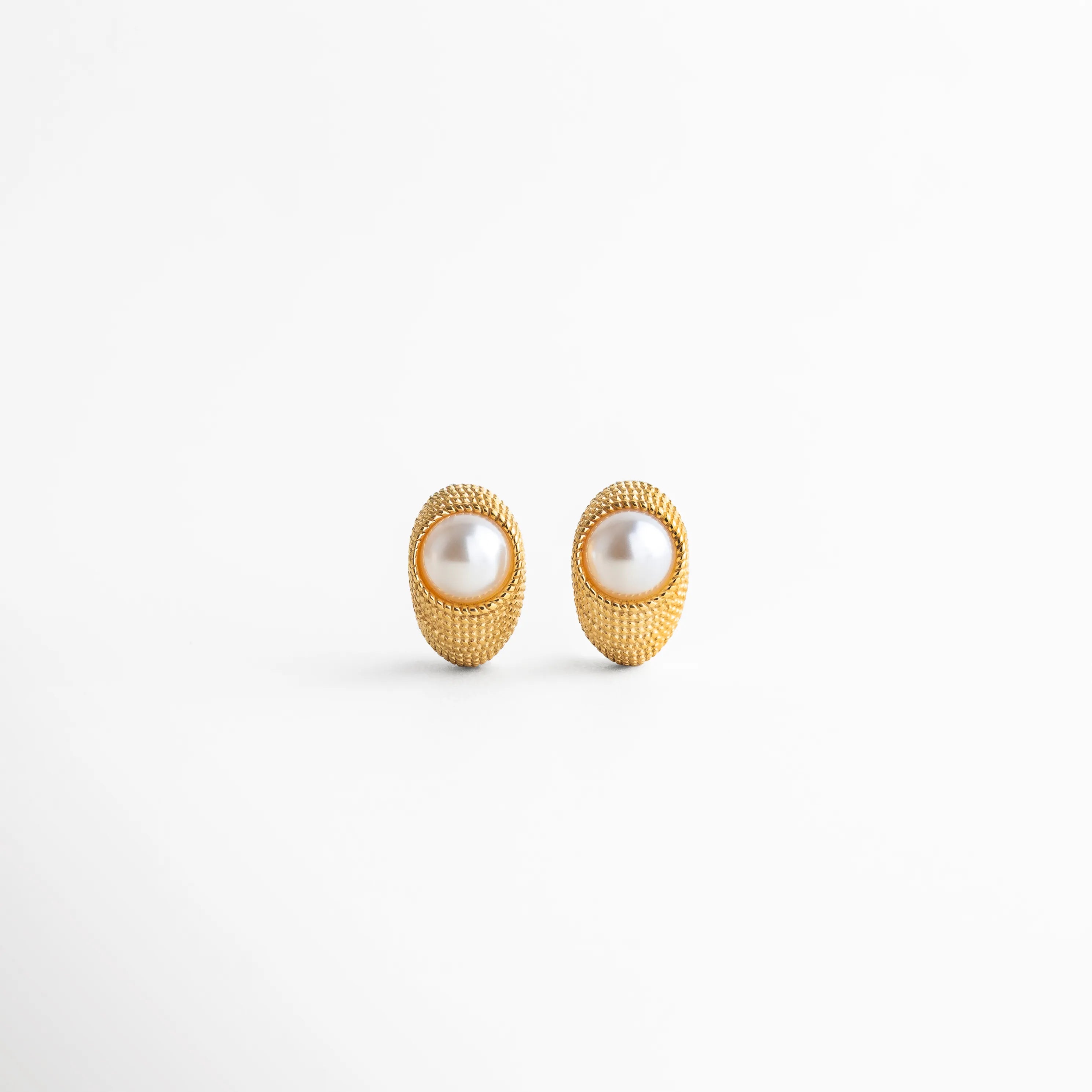 Aretes Bimba dorados con perla sintética, diseño ovalado con textura elegante en acero inoxidable, Par de aretes dorados con incrustación de perla sintética, estilo moderno con acabado texturizado, Aretes ovalados con perla sintética central, chapa de oro 18K y diseño sofisticado, Pendientes dorados con perla sintética y textura tipo joyería imperial, vista frontal, Aretes Bimba con acabado dorado y perla sintética, diseño elegante de 2.5 cm