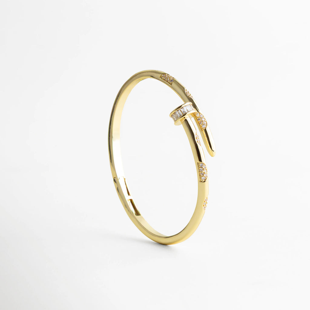 pulsera dorada en posición vertical resaltando el diseño tipo clavo y las zirconias brillantes, con fondo blanco