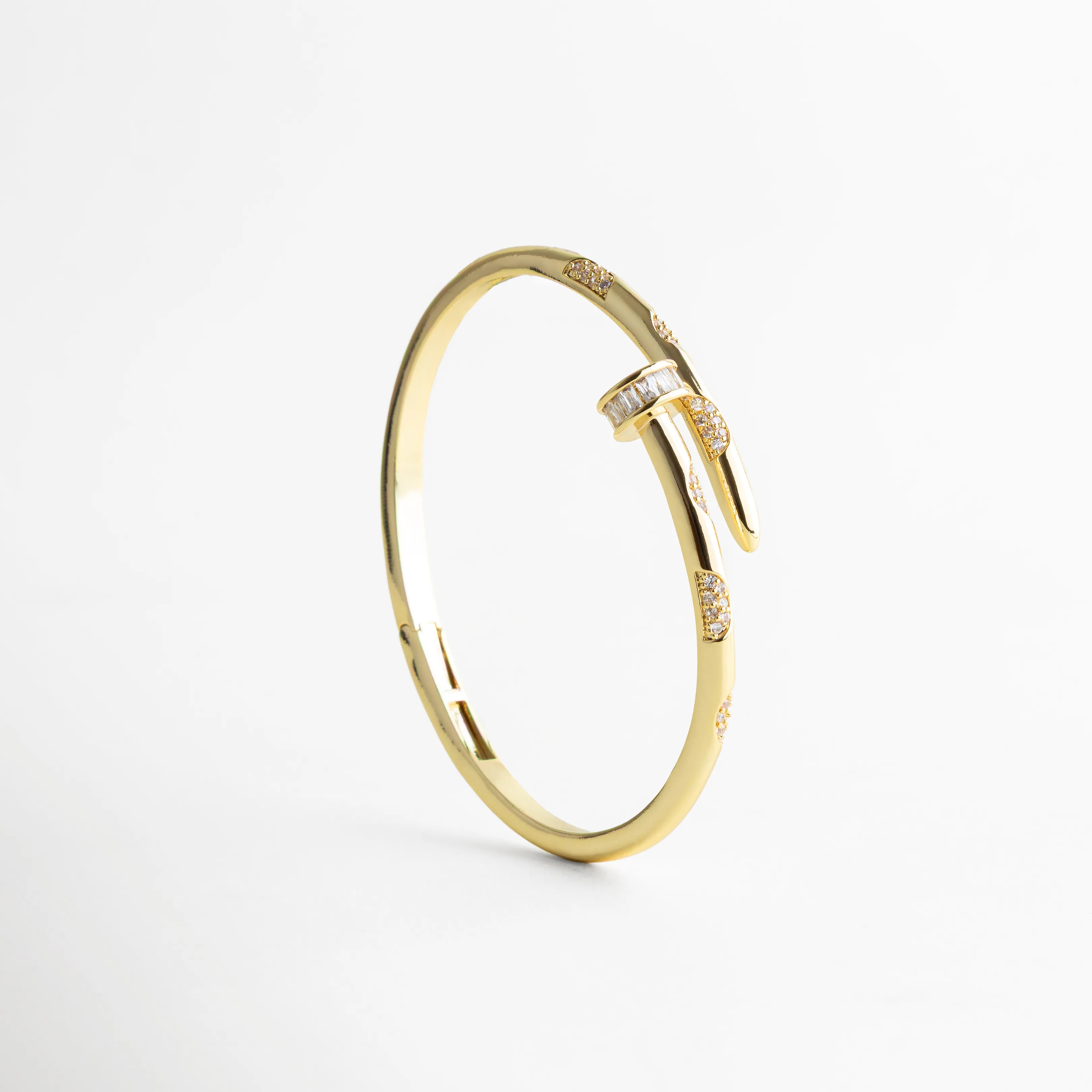 pulsera dorada en posición vertical resaltando el diseño tipo clavo y las zirconias brillantes, con fondo blanco