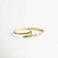 pulsera dorada estilo clavo abierta al frente con zirconias incrustadas en puntos estratégicos, sobre fondo blanco minimalista