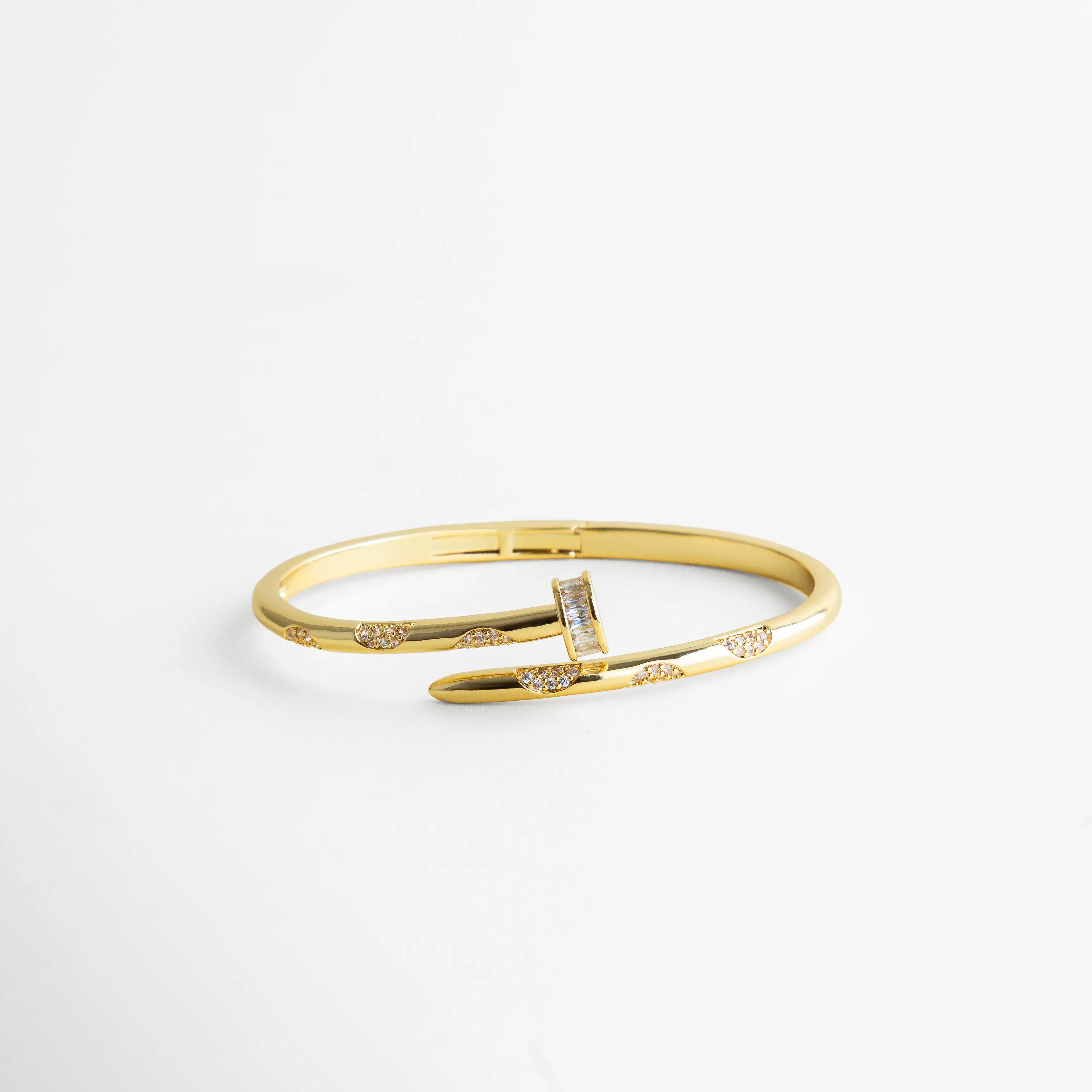 pulsera dorada estilo clavo abierta al frente con zirconias incrustadas en puntos estratégicos, sobre fondo blanco minimalista