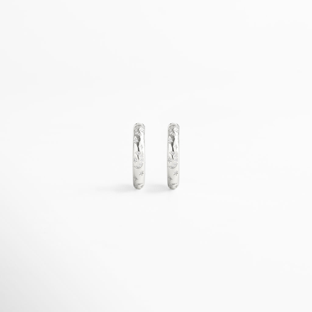 Vista frontal de aretes de aro fabricados en cobre con baño de oro blanco 18K, acabado brillante con diamantes de imitación y grabados de estrellas, diseño minimalista y versátil de 2 x 0.5 cm ideal para looks sofisticados y casuales.