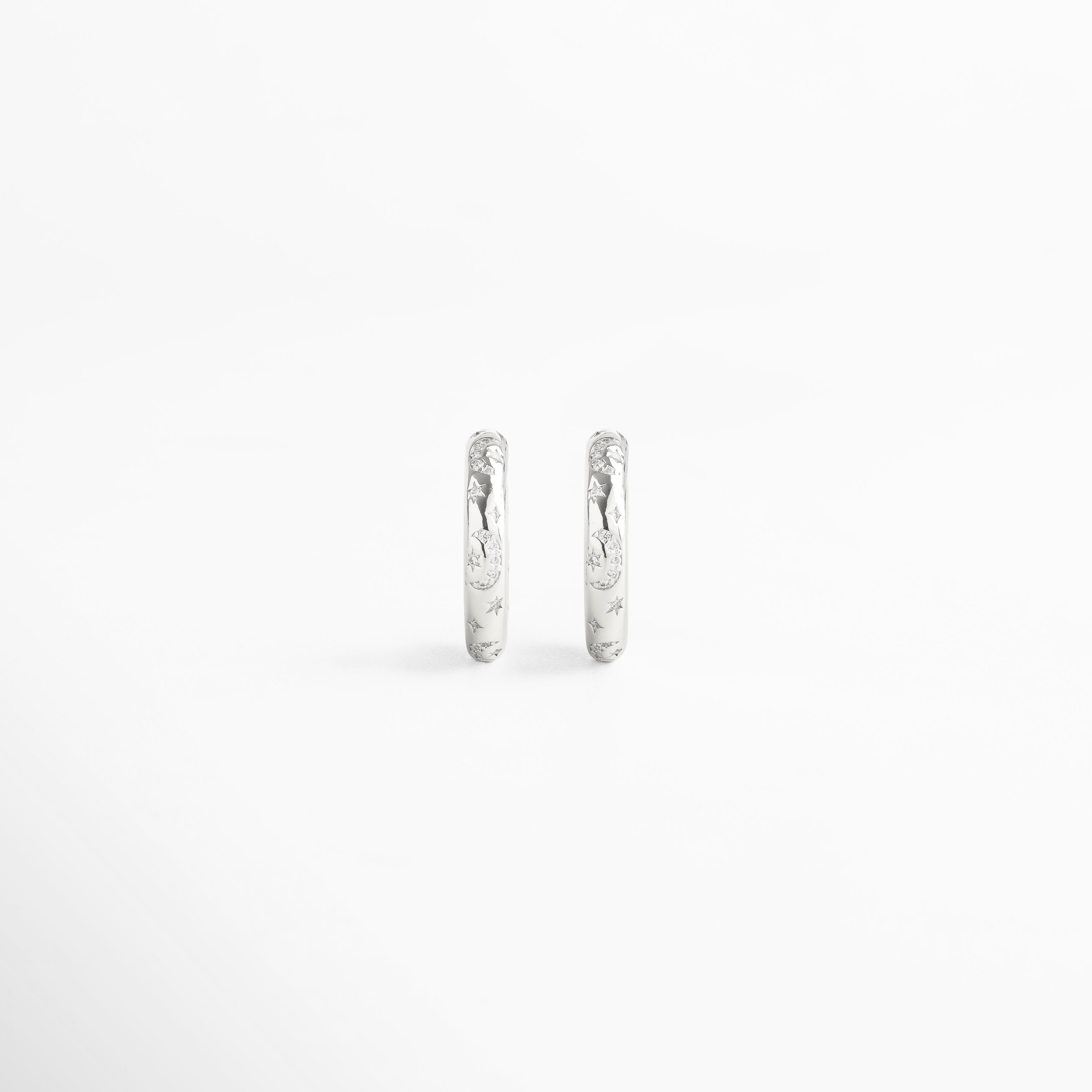 Vista frontal de aretes de aro fabricados en cobre con baño de oro blanco 18K, acabado brillante con diamantes de imitación y grabados de estrellas, diseño minimalista y versátil de 2 x 0.5 cm ideal para looks sofisticados y casuales.