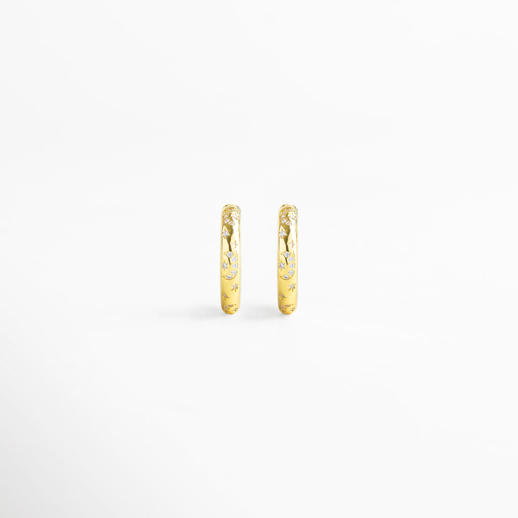 Vista frontal de aretes de aro fabricados en cobre con baño de oro 18K, acabado brillante con diamantes de imitación y grabados de estrellas, diseño minimalista y versátil de 2 x 0.5 cm ideal para looks sofisticados y casuales.