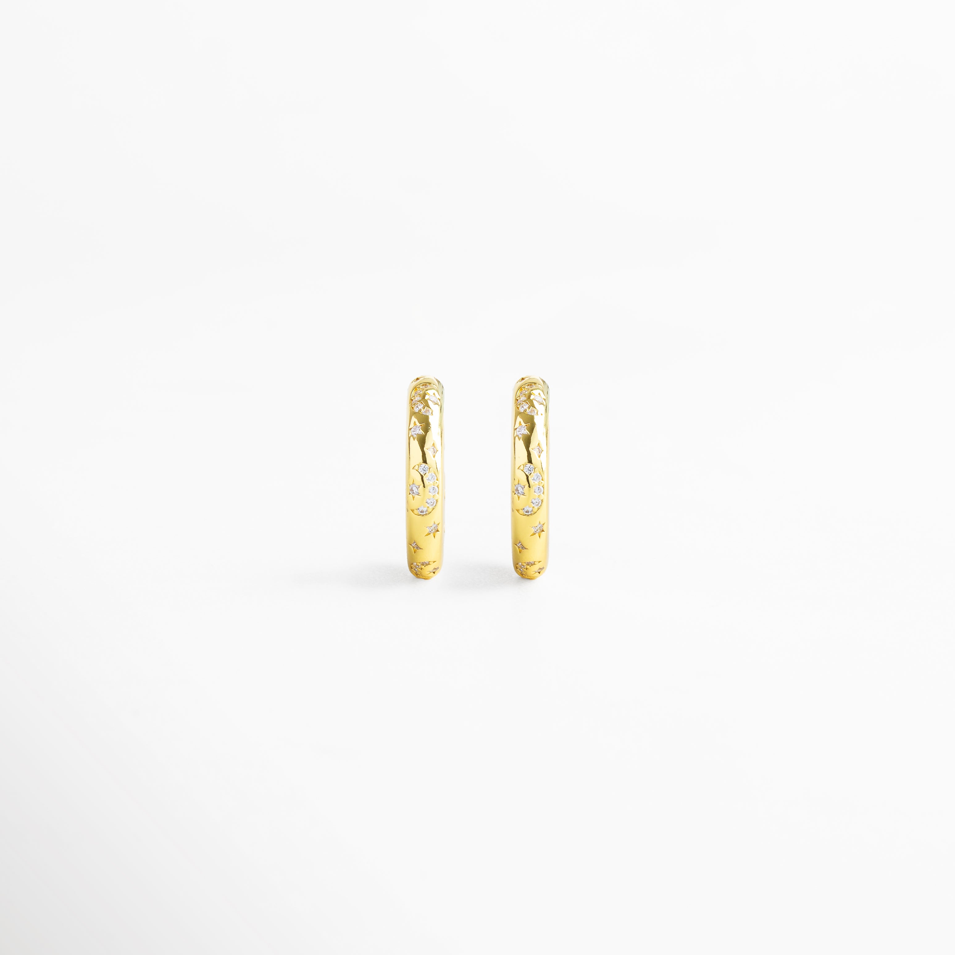 Vista frontal de aretes de aro fabricados en cobre con baño de oro 18K, acabado brillante con diamantes de imitación y grabados de estrellas, diseño minimalista y versátil de 2 x 0.5 cm ideal para looks sofisticados y casuales.