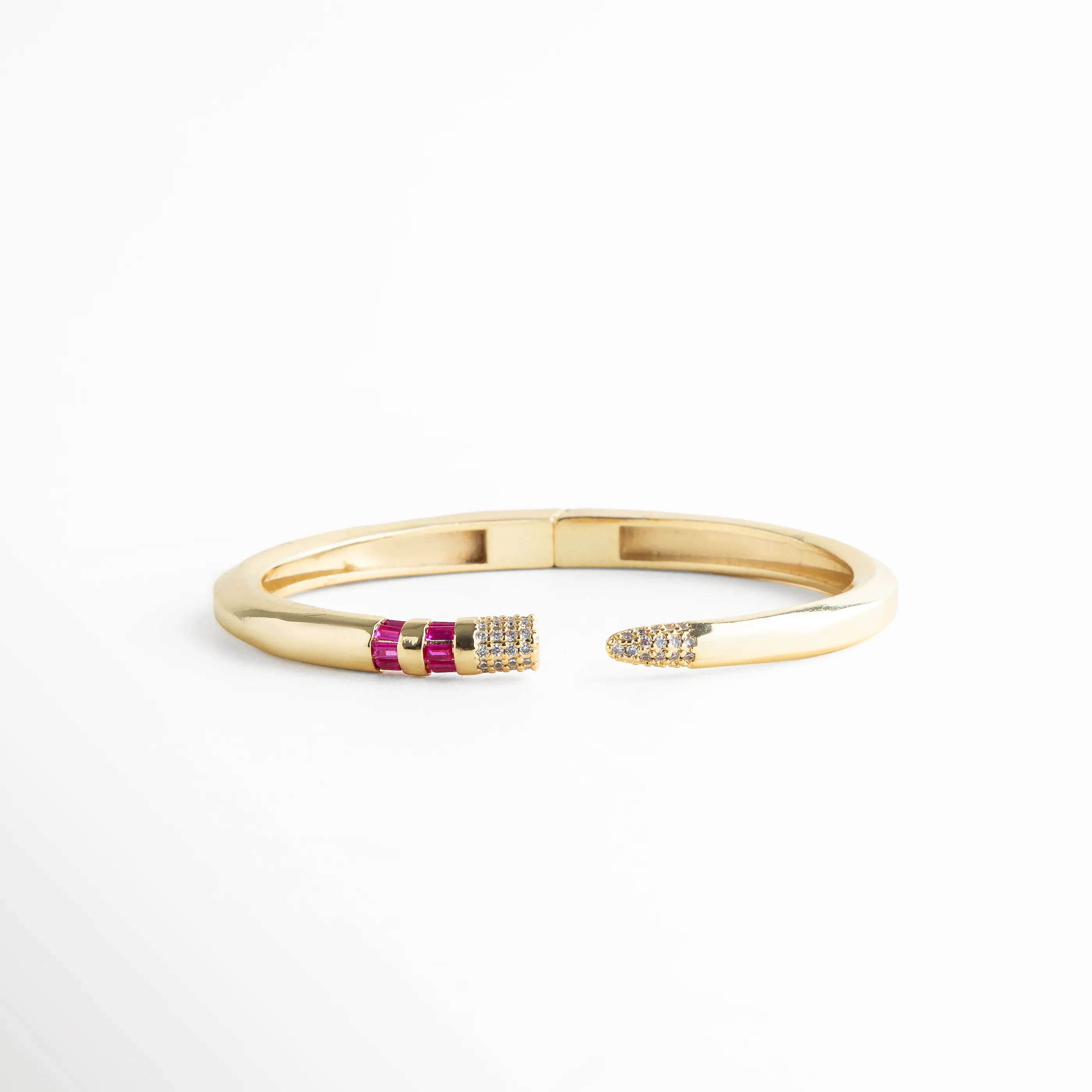 Perspectiva angular del brazalete resaltando el contraste entre el oro y las circonias fucsia, Brazalete de moda con puntas brillantes y piedras baguette, vista de tres cuartos, 
Joyería contemporánea: pulsera rígida dorada con destellos de circonia rosa intenso, Vista en ángulo que muestra el relieve de las piedras incrustadas en el brazalete dorado, Pulsera tipo joya de diseñador con acabado premium y detalles de cristales baguette.