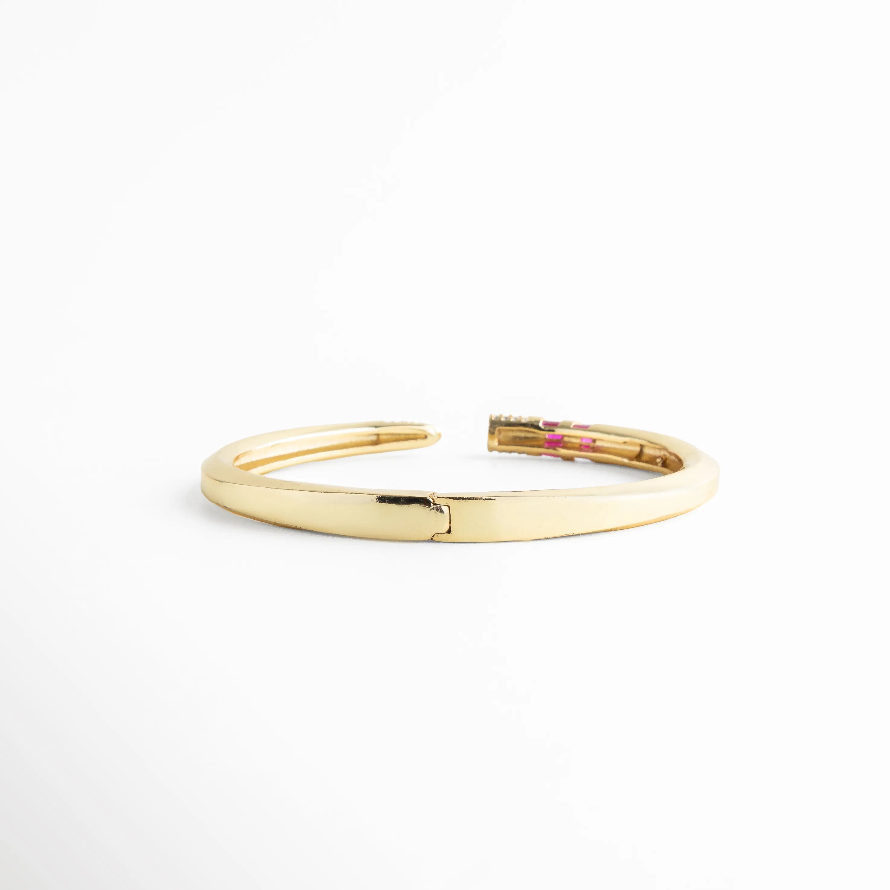 Vista posterior del brazalete dorado mostrando el sistema de bisagra para fácil apertura, Detalle técnico del mecanismo de cierre y apertura del brazalete rígido de oro 18K, Pulsera dorada lisa por la parte posterior con acabado espejo y alta calidad de enchapado, Estructura de brazalete con bisagra central, garantizando comodidad y ajuste seguro, Parte trasera de pulsera de lujo con recubrimiento de oro 18K y diseño minimalista.