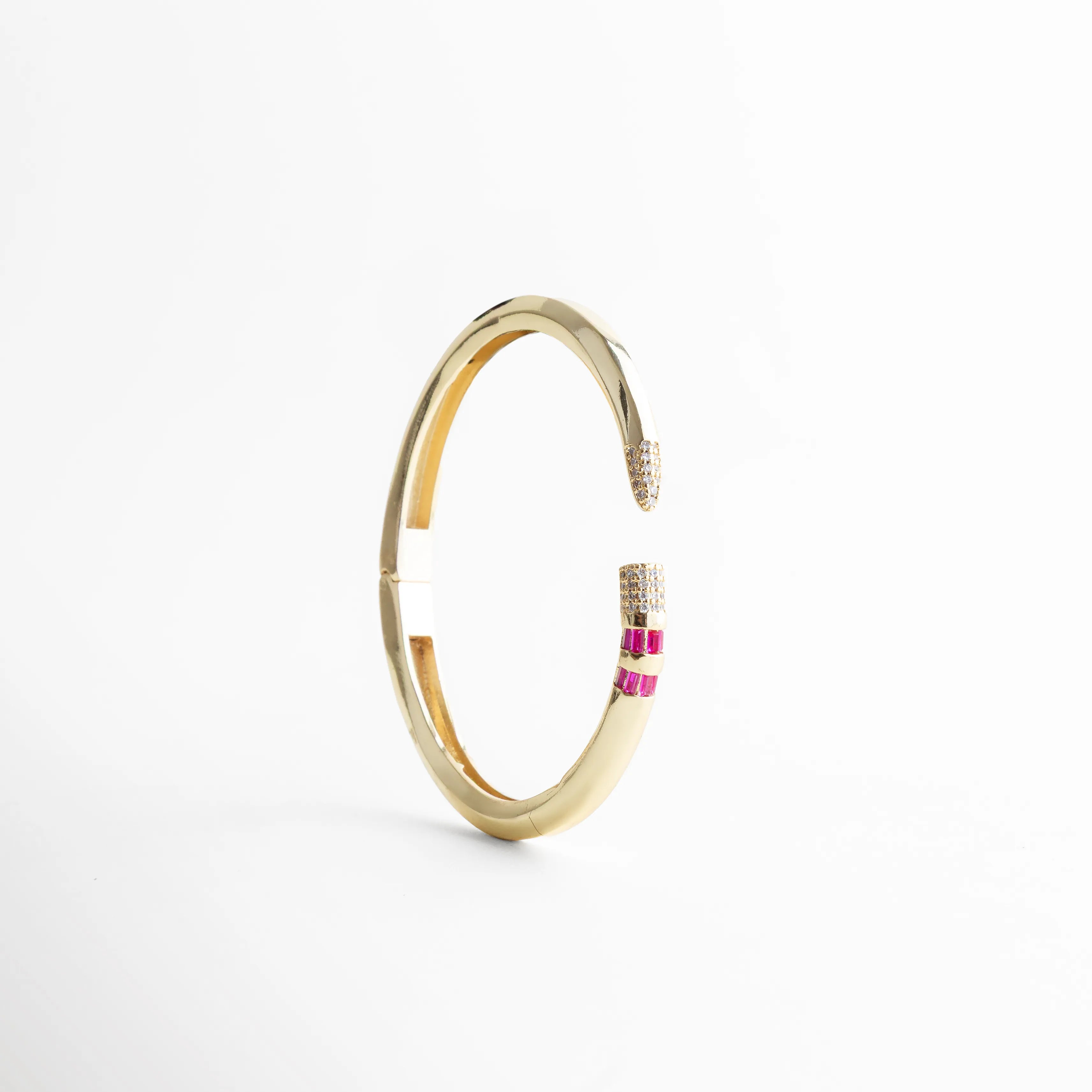 Vista lateral del brazalete circular dorado resaltando su estructura rígida y ergonómica, Pulsera de oro 18K con diámetro de 6.5 cm y diseño moderno de puntas encontradas, Brazalete con bisagra invisible que muestra la curvatura perfecta y el brillo del acabado, Accesorio de muñeca dorado con piedras brillantes, vista vertical de perfil delgado, Brazalete de cobre enchapado en oro con detalle de micro-pavé en los extremos.