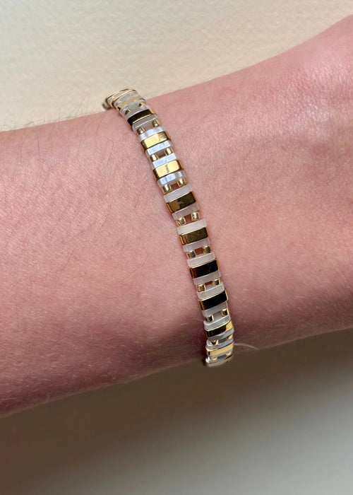 Pulsera dorada con rectángulos blancos y negros, diseño minimalista elegante, Pulsera elástica de cuentas rectangulares doradas y blancas, joya moderna y sofisticada, Pulsera rectangular en dorado con detalles blancos y negros, estilo atemporal.