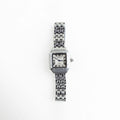 Reloj de mujer con carátula cuadrada y acabado en oro blanco, diseño elegante y sofisticado, Vista frontal de reloj femenino en acero inoxidable con estilo refinado y brillo sutil, Reloj elegante para mujer con carátula pequeña y acabado brillante en oro blanco, Carátula de reloj femenino con diseño moderno y acabado en acero inoxidable en tono plata, Reloj de mujer sofisticado con acabado en oro blanco y estilo delicado para uso diario.