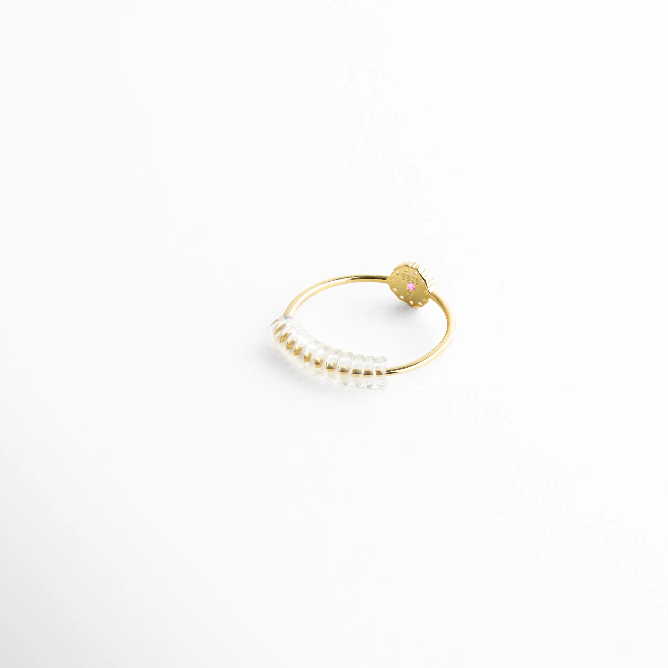 Anillo minimalista con piedra color rubí y banda delgada, acompañado de un resorte ajustable que asegura una sujeción cómoda. La fotografía resalta su acabado pulido y la transparencia del accesorio, pensado para quienes buscan comodidad sin comprometer el diseño.