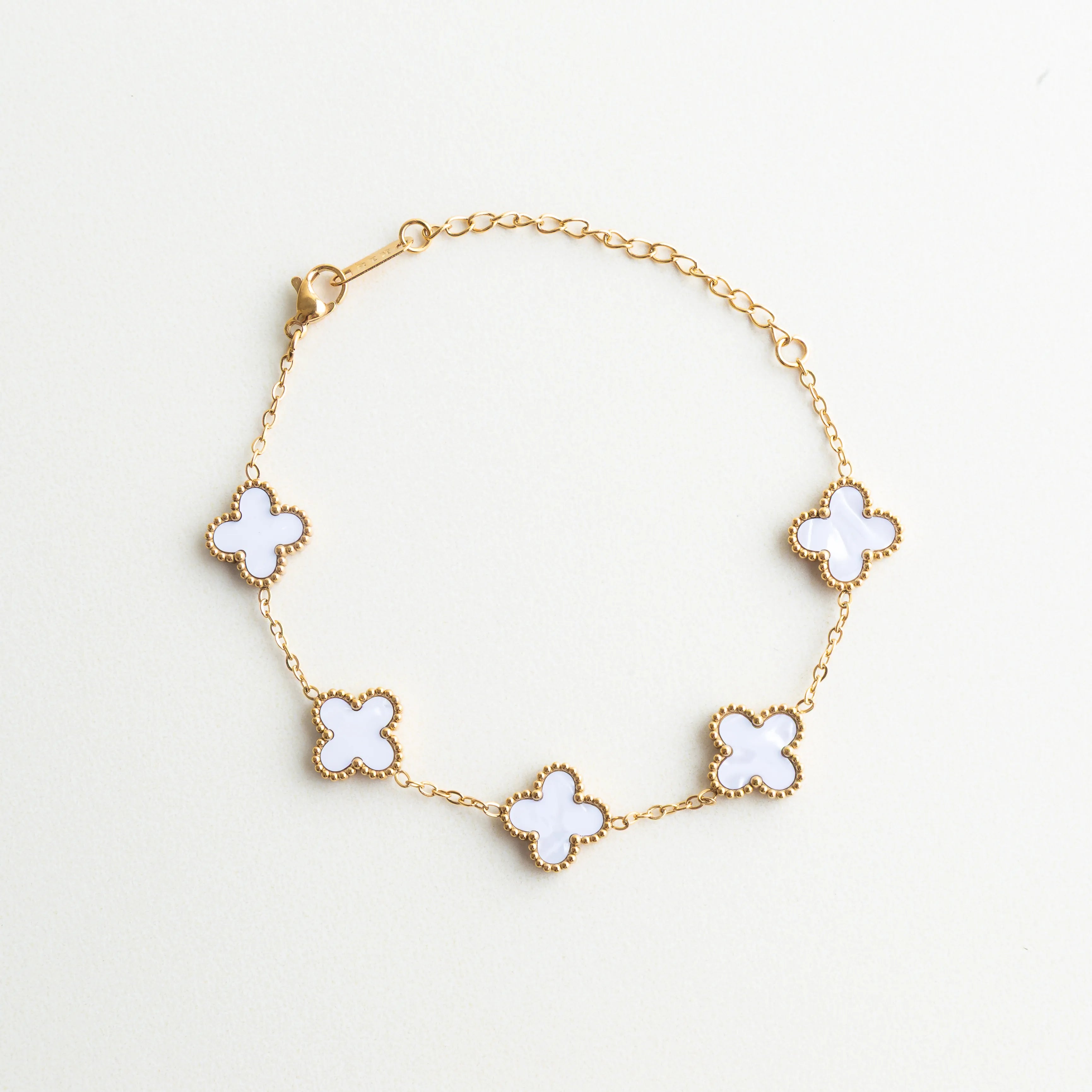 Pulsera dorada con dijes de trébol blanco y acabado elegante, Pulsera de acero inoxidable con tréboles de nácar y baño en oro 18K, Pulsera femenina con dijes de trébol blanco y diseño delicado, Pulsera elegante con detalles de trébol y piedras de nácar, Pulsera completa con tréboles blancos y estilo sofisticado